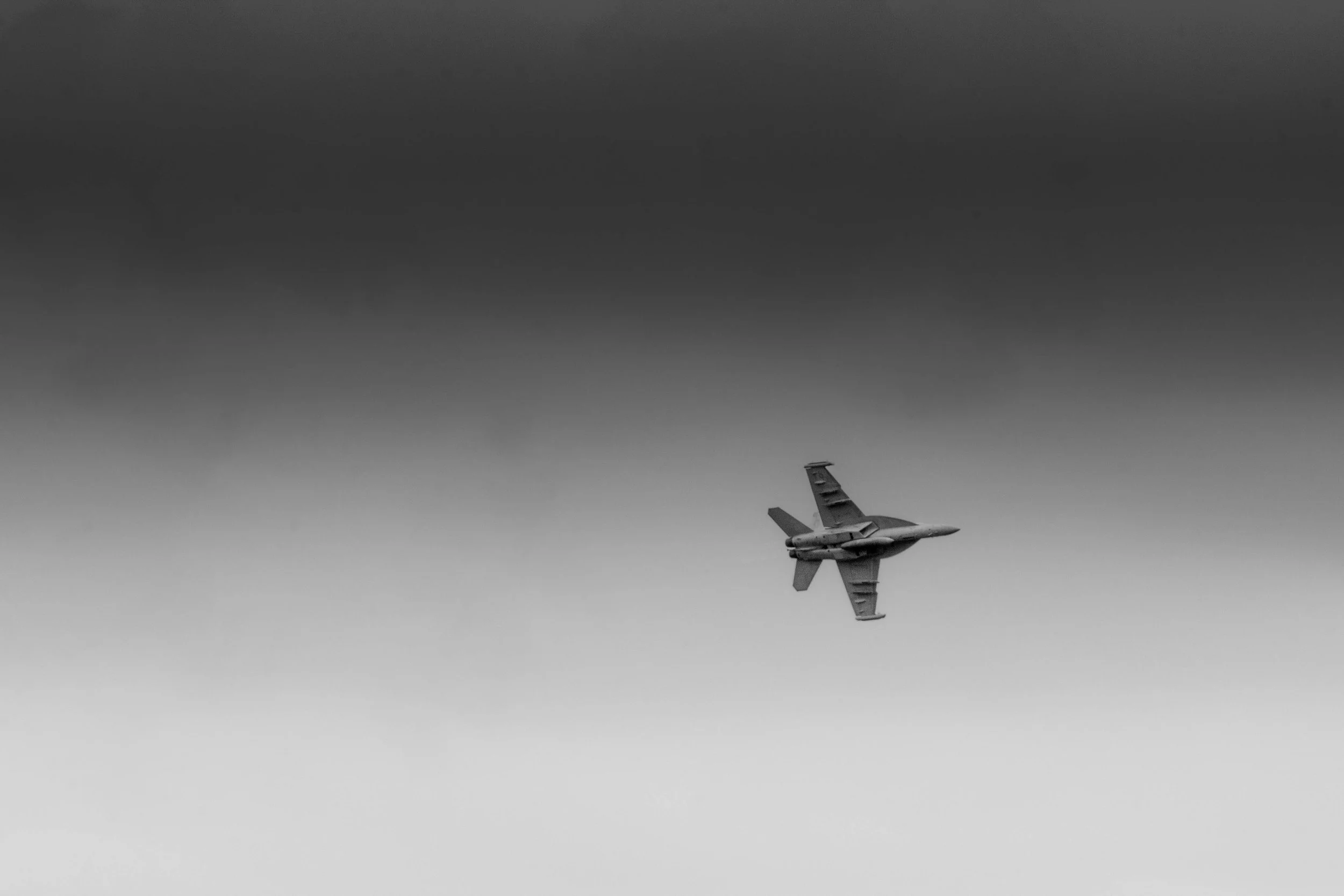 A fighter jet flying through a cloudy sky in black and white.