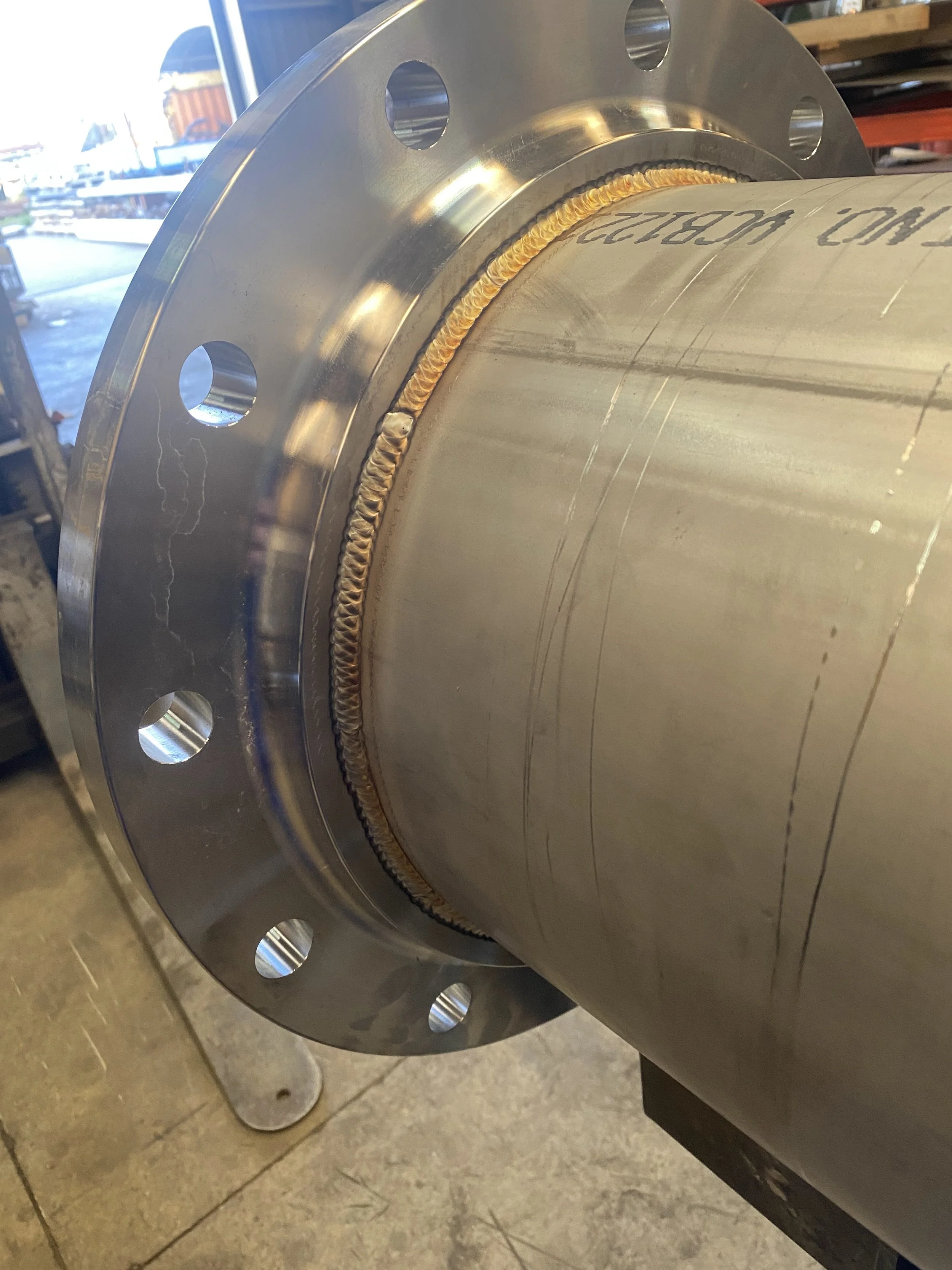 Close-up of a large metal pipe with a flange and a welded seam, prepared for assembly or installation in an industrial setting.