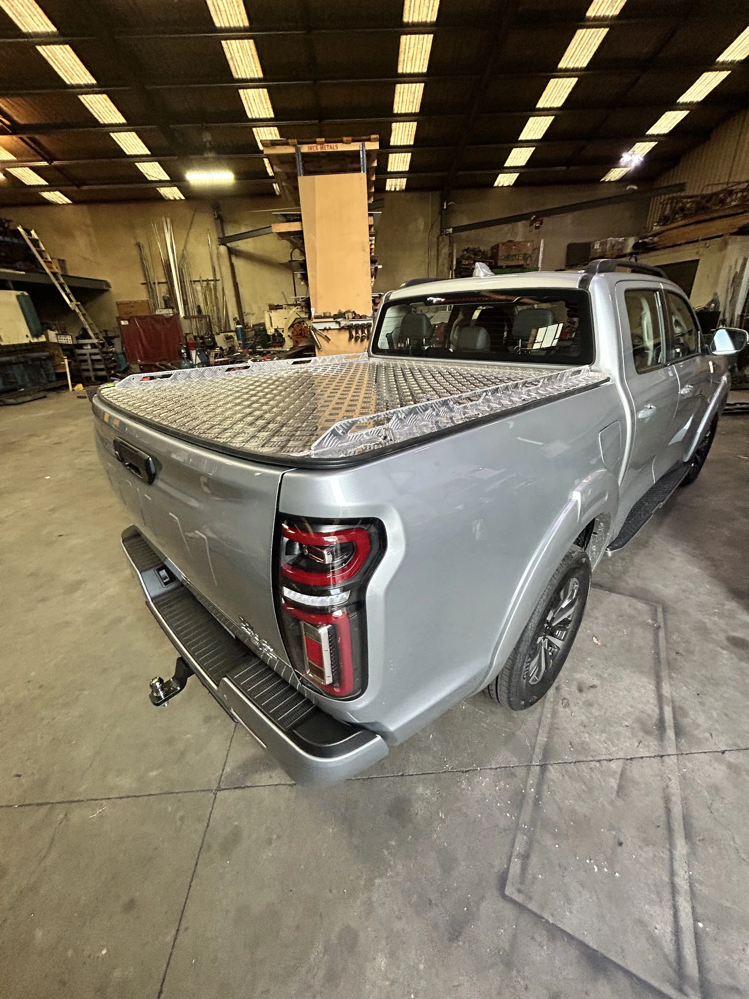 A silver pickup truck with a diamond plate bed cover inside a workshop or garage.