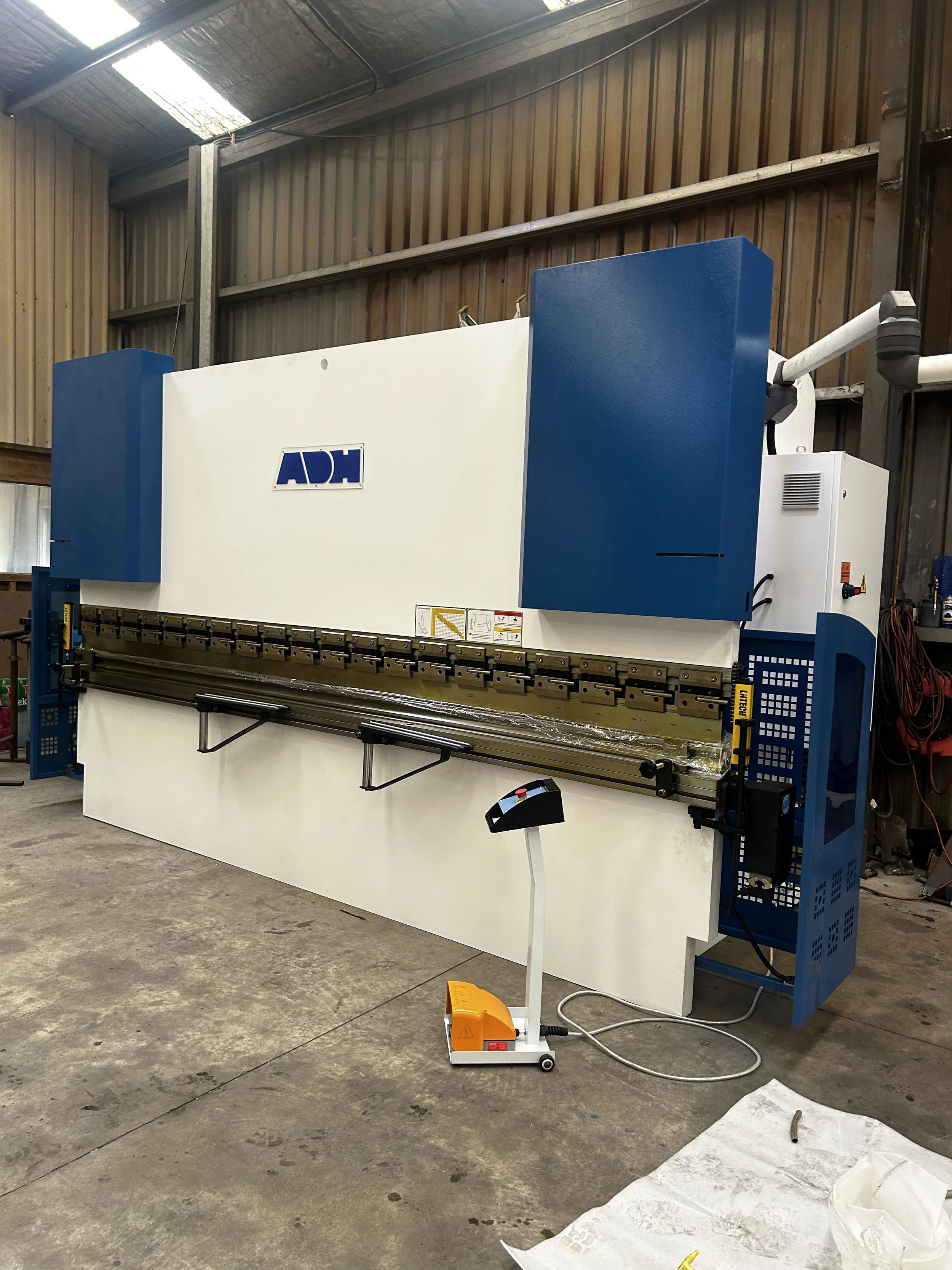A large industrial machine with the label 'ADH' in a warehouse setting, with a long metal arm and a control panel, and a robotic arm attached to it.