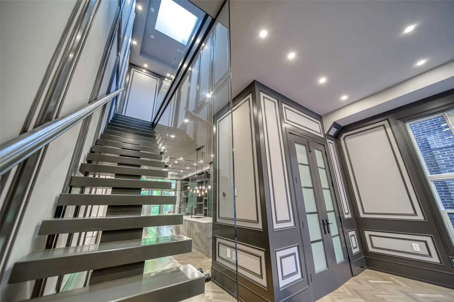 Modern interior with floating staircase, gray paneled walls with decorative molding, and large windows in a well-lit room.