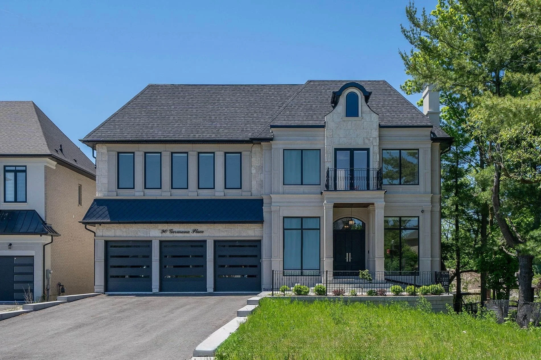 Modern, multi-story house with a dark gray roof, large windows, and a black front door, surrounded by green lawn and trees