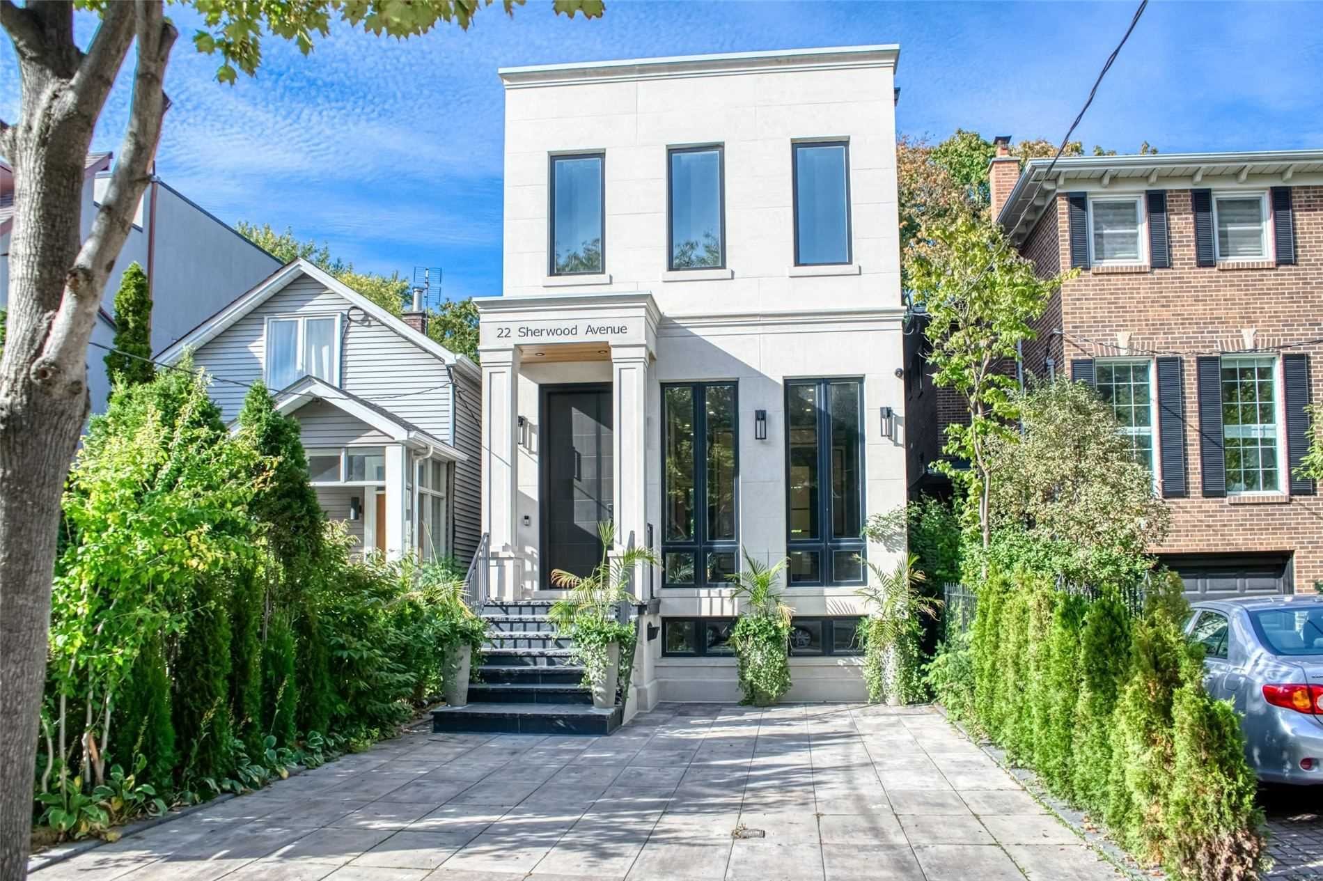 Modern white townhouse with large windows, steps leading up to the entrance, and surrounding greenery, located at 22 Sherwood Avenue.