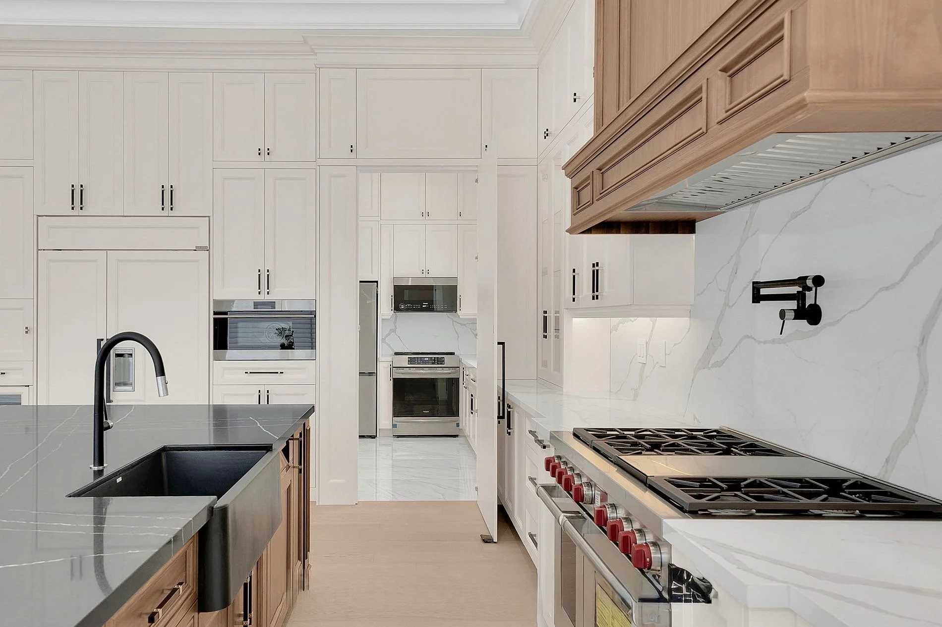 Modern kitchen with white and wood cabinetry, marble countertops, black faucet, black stovetop, and stainless steel appliances.