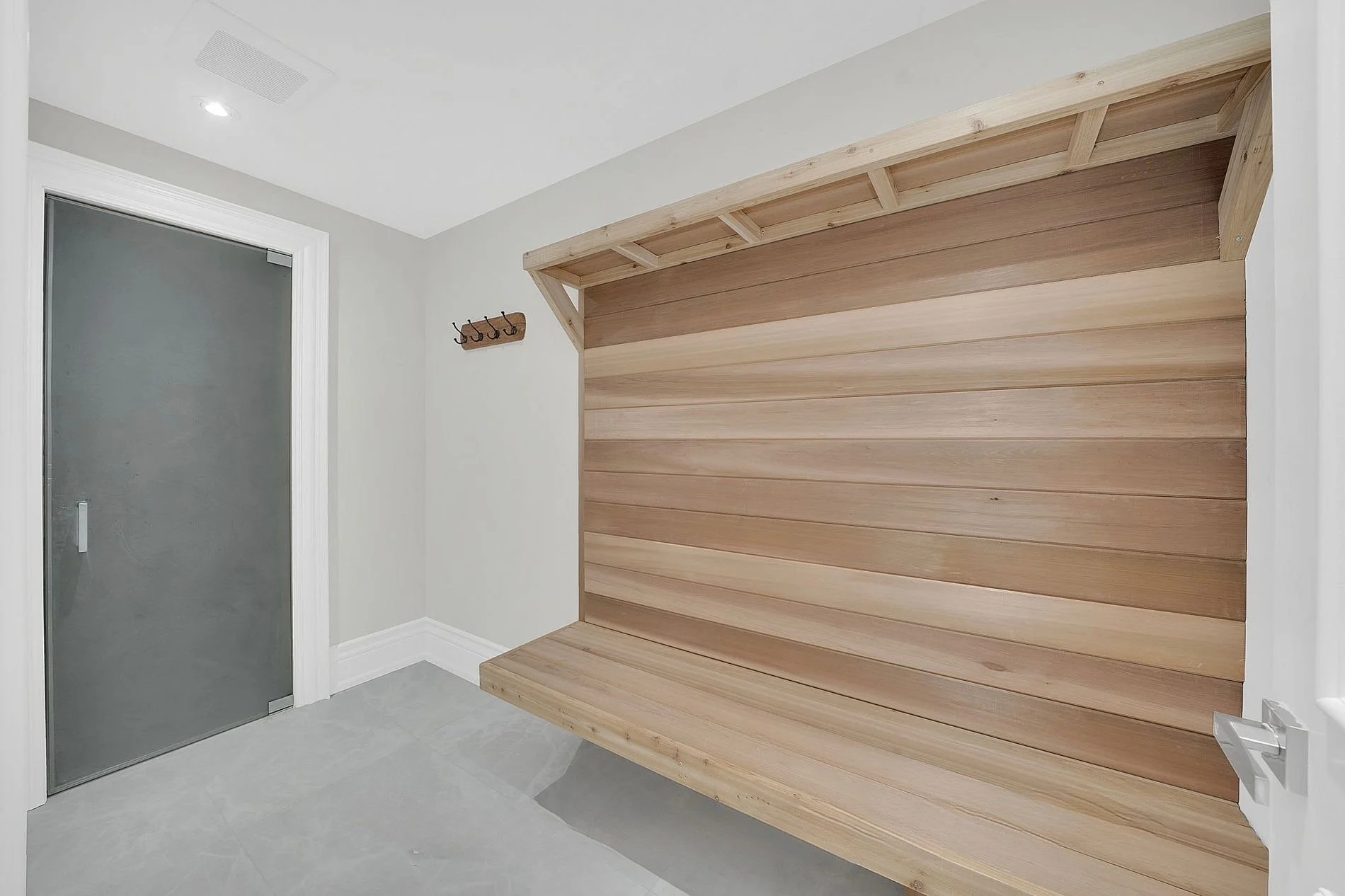 A modern entryway with a gray door, a coat hook on the wall, and a wooden bench with a slatted back panel.