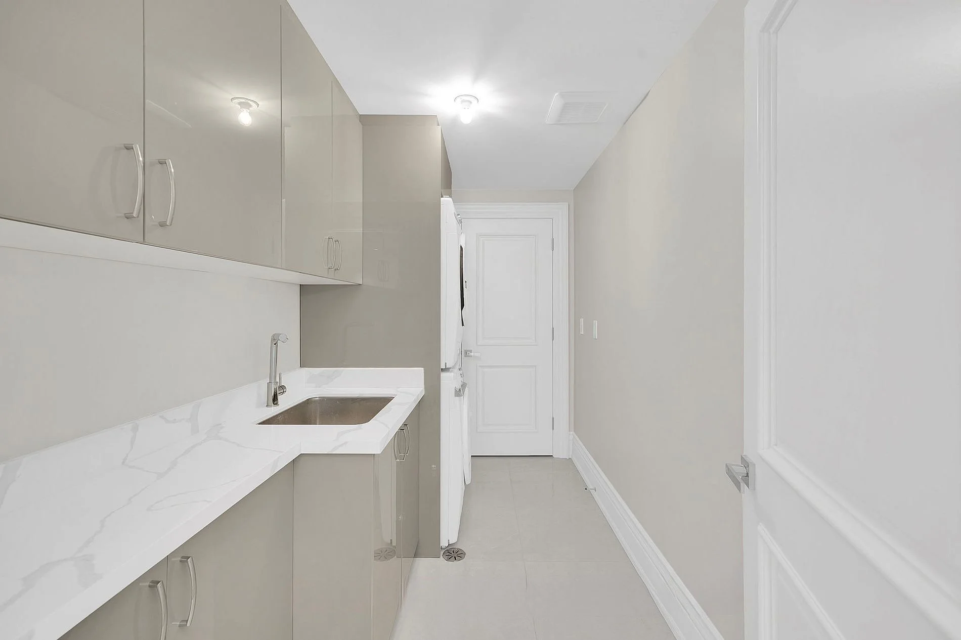 Laundry room with gray cabinets, white marble countertop, small sink, and a white door.