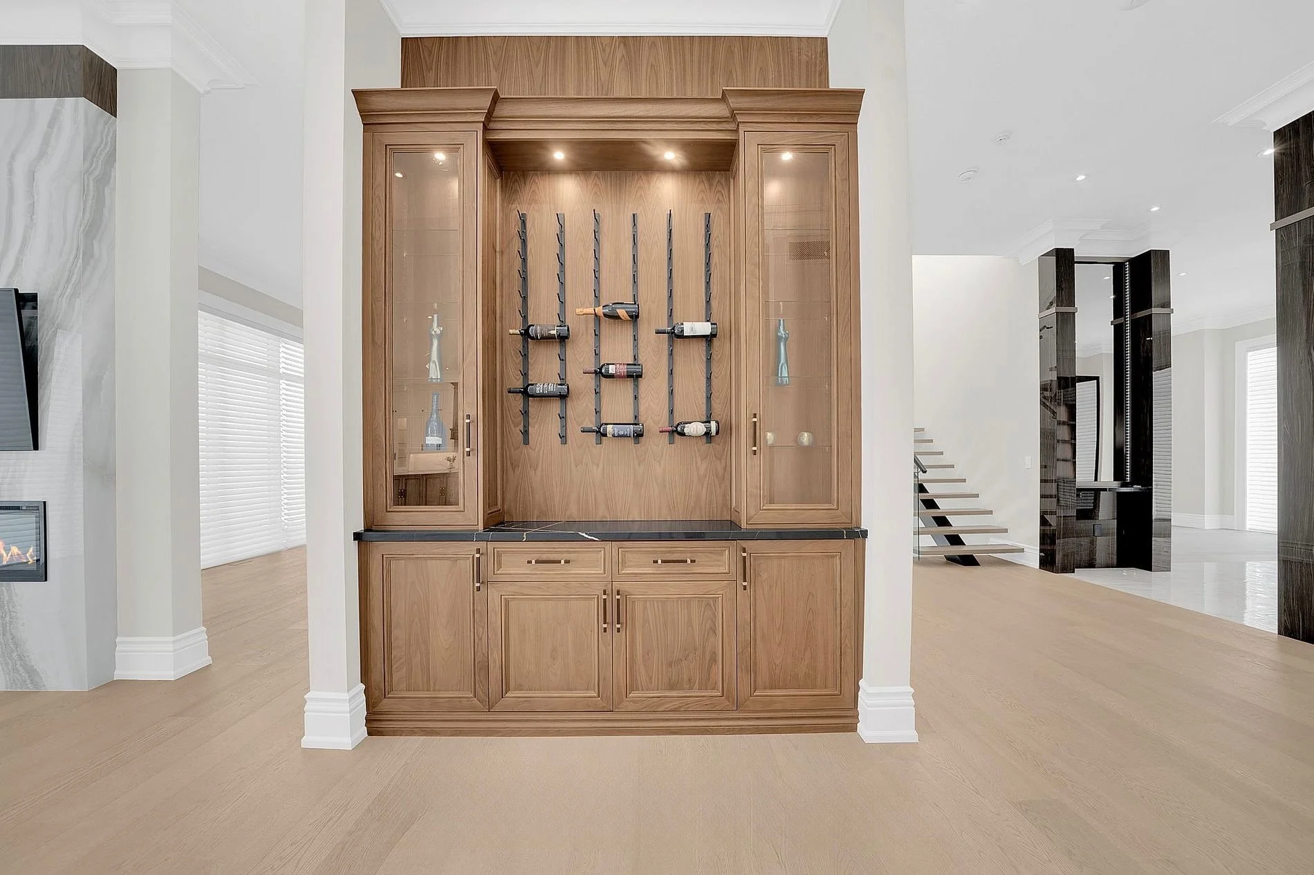 Built-in wooden cabinet with wine rack, glass doors, and shelves in a modern open-concept living space.