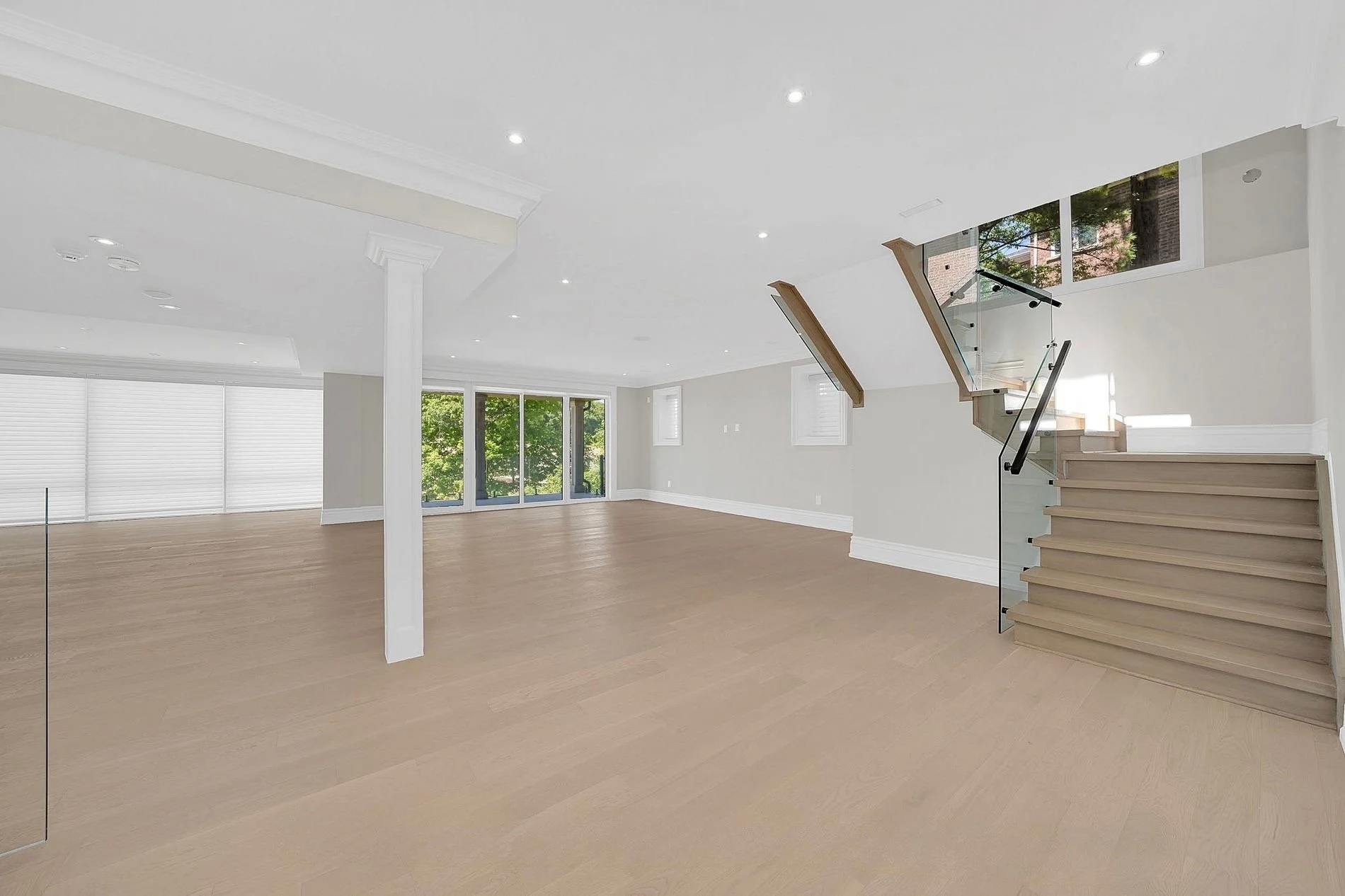 Empty modern living space with hardwood floors, large windows, staircase, and ceiling lights.