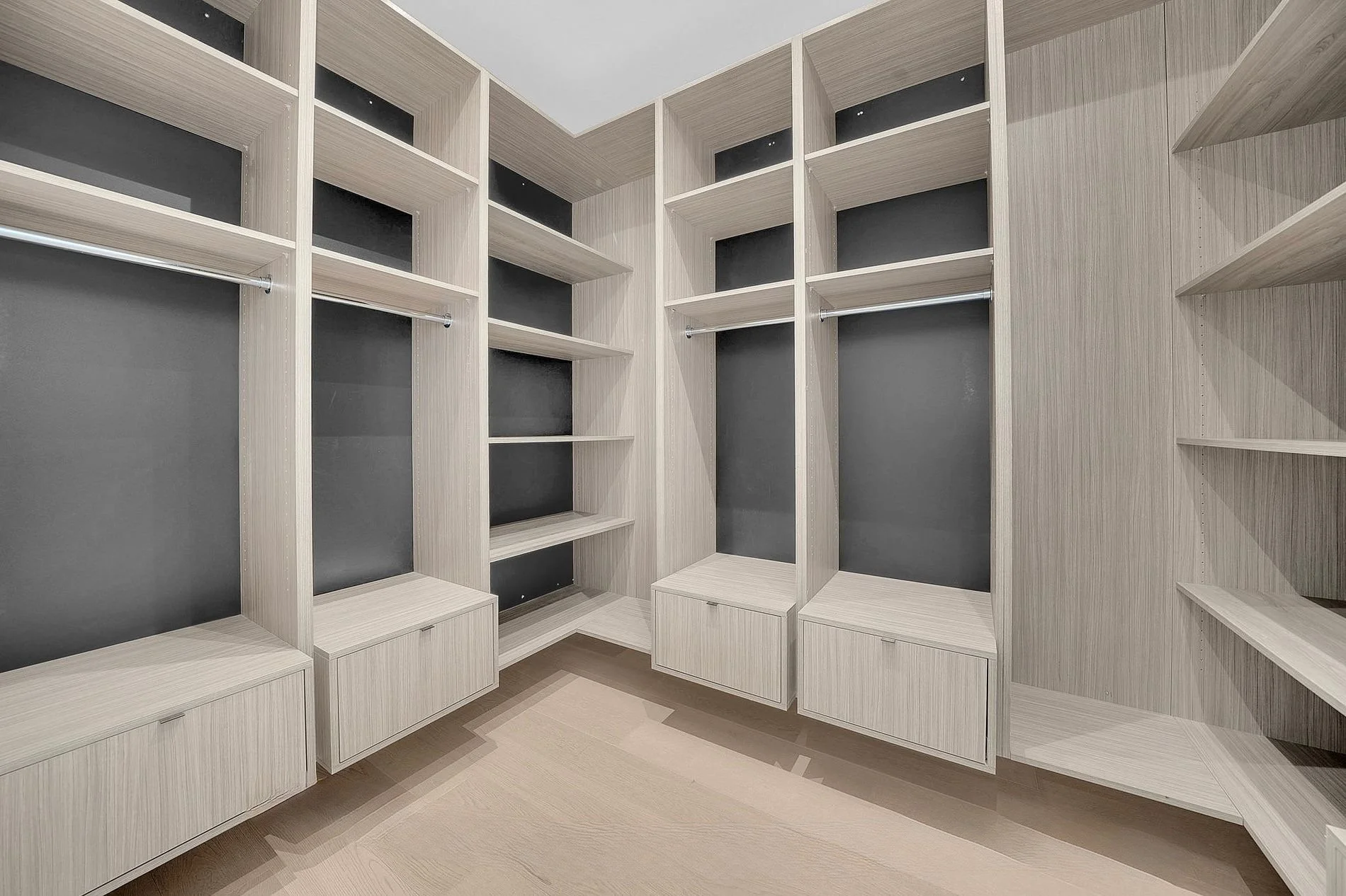 Empty walk-in closet with light wood shelving and drawers, and gray painted wall accents.