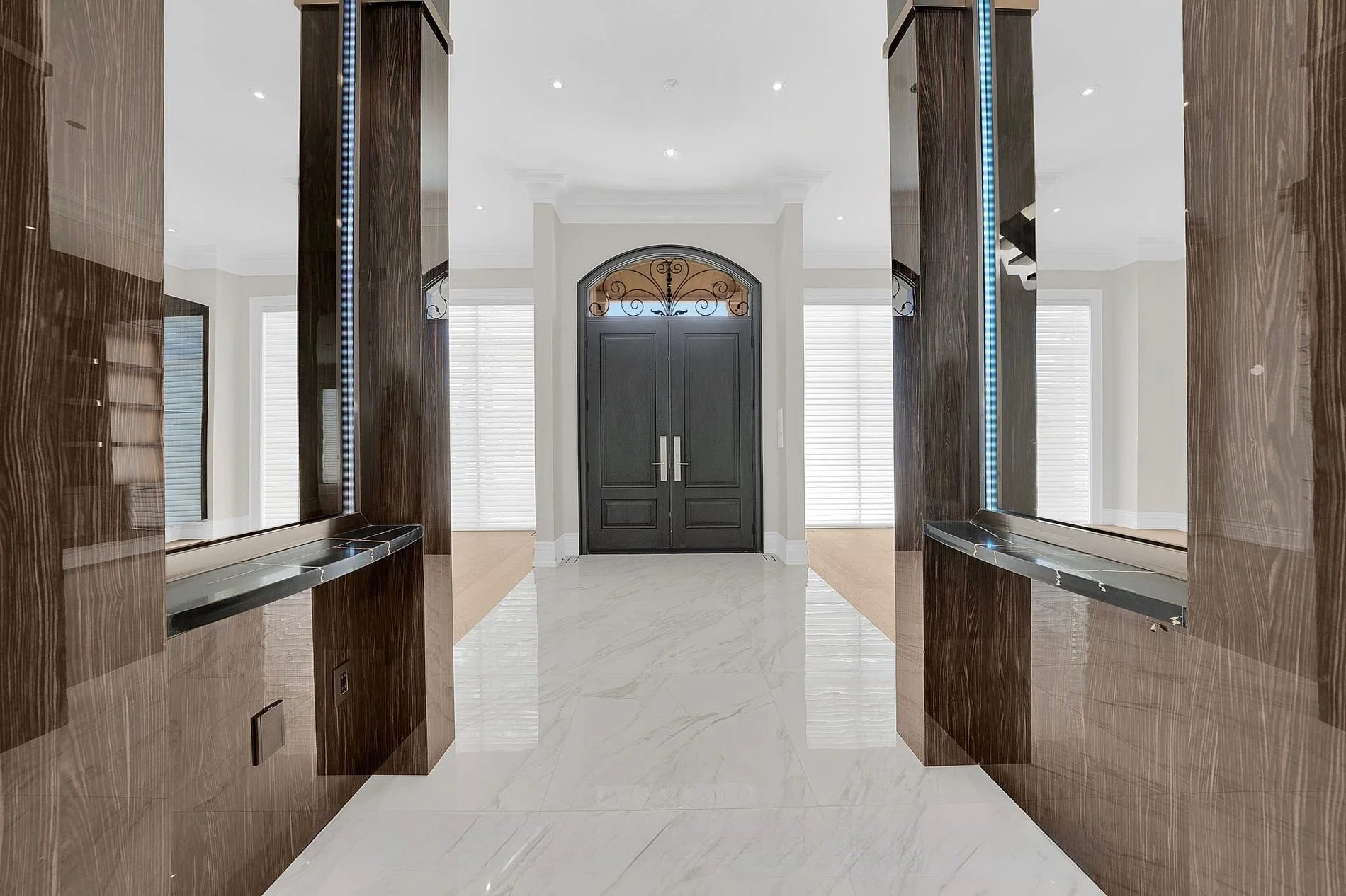 Elegant entrance with polished marble floor, wooden and mirrored walls, and a black double door with decorative ironwork above.