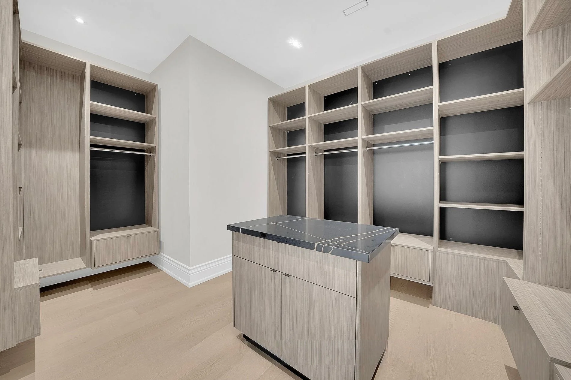 Empty walk-in closet with built-in wooden shelves, drawers, and a small central island with a black marble top.