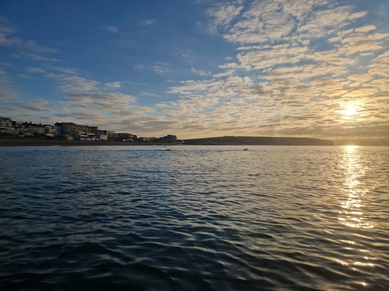 Sunset over the ocean with cloudy sky and distant shoreline with buildings.