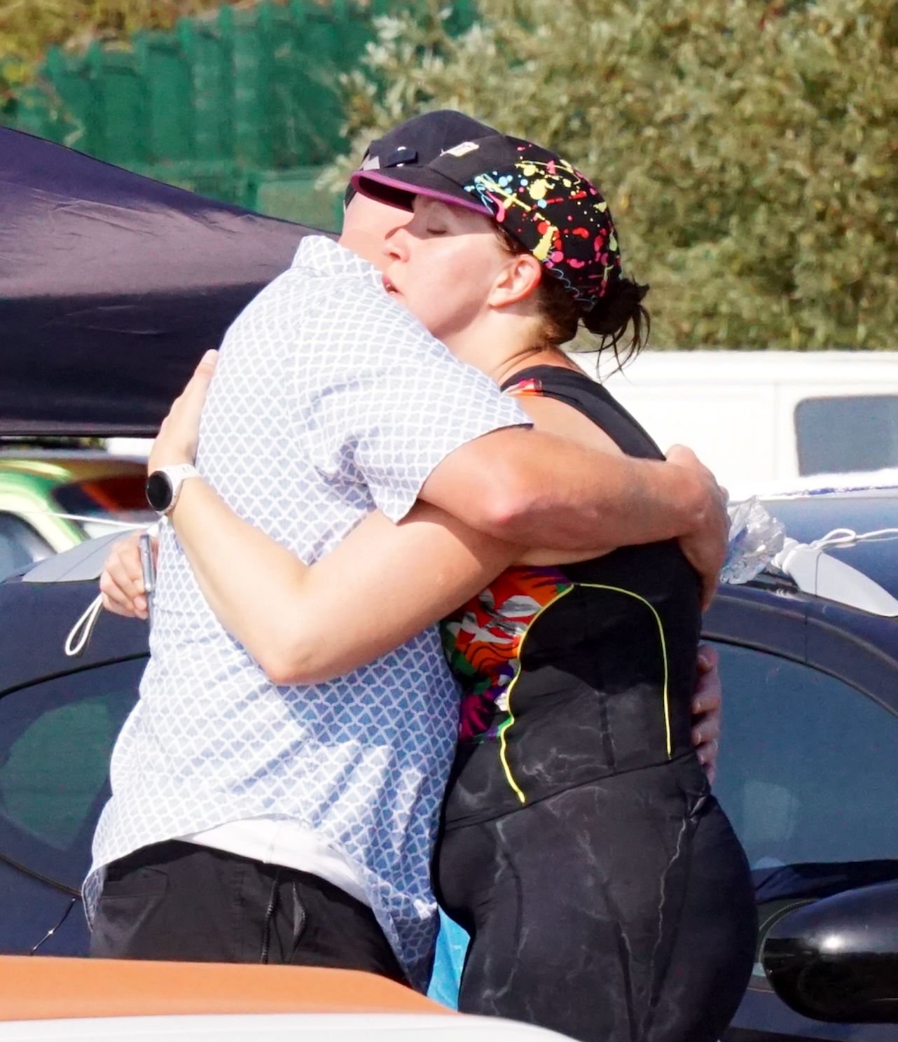 Two women hugging each other warmly outdoors, one with a cap, and a city street background.