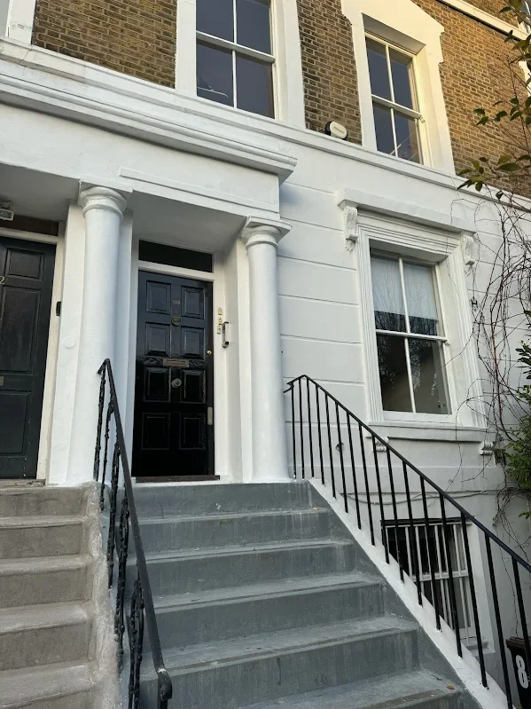 The front entrance of a brick and white house with a black door, white columns, and black iron railing on concrete stairs.