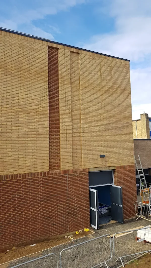 Construction site with a brick building and open double doors, construction tools on the ground, scaffolding, and fencing.
