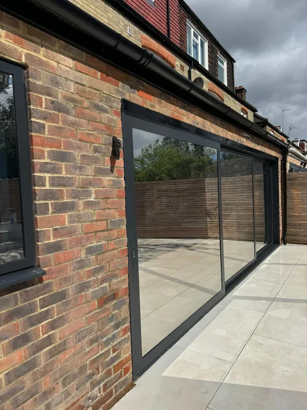 Modern dwelling with a large glass sliding door on a brick wall, overlooking a courtyard with a wooden fence and tiled patio.