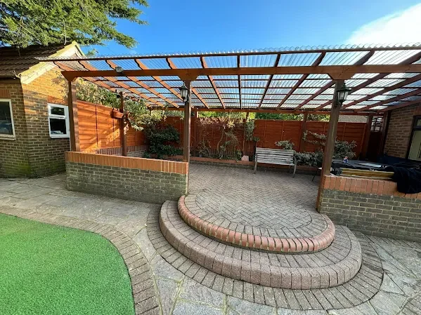 Backyard with a brick patio, a curved step, a wooden and metal pergola, a bench, and a wooden privacy fence.