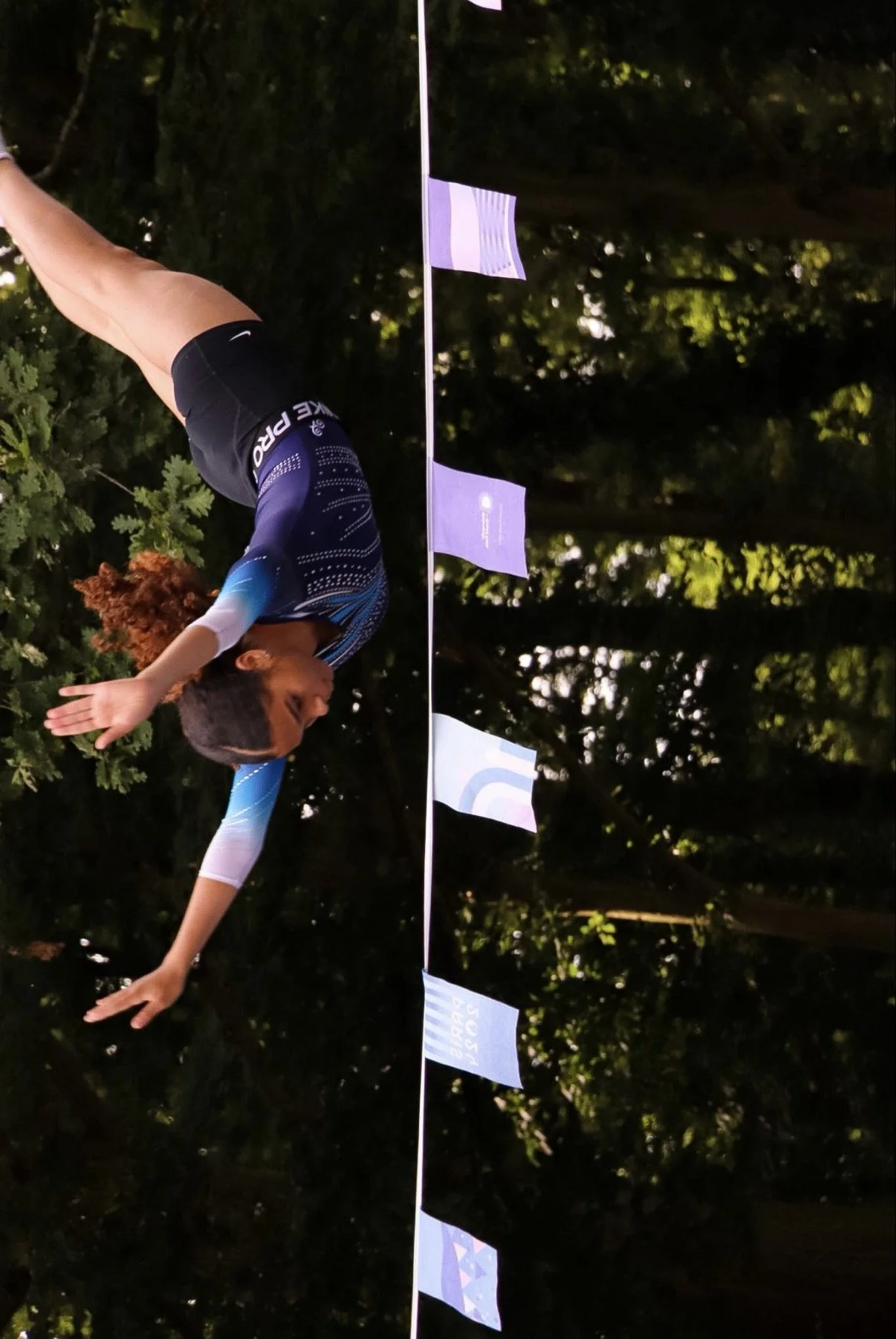 Photographie d'une athlète gymnaste en tenue de sport qui effectue une acrobatie en l'air, dans un parc en Seine-Saint-Denis pour les jeux olympiques 2024. 