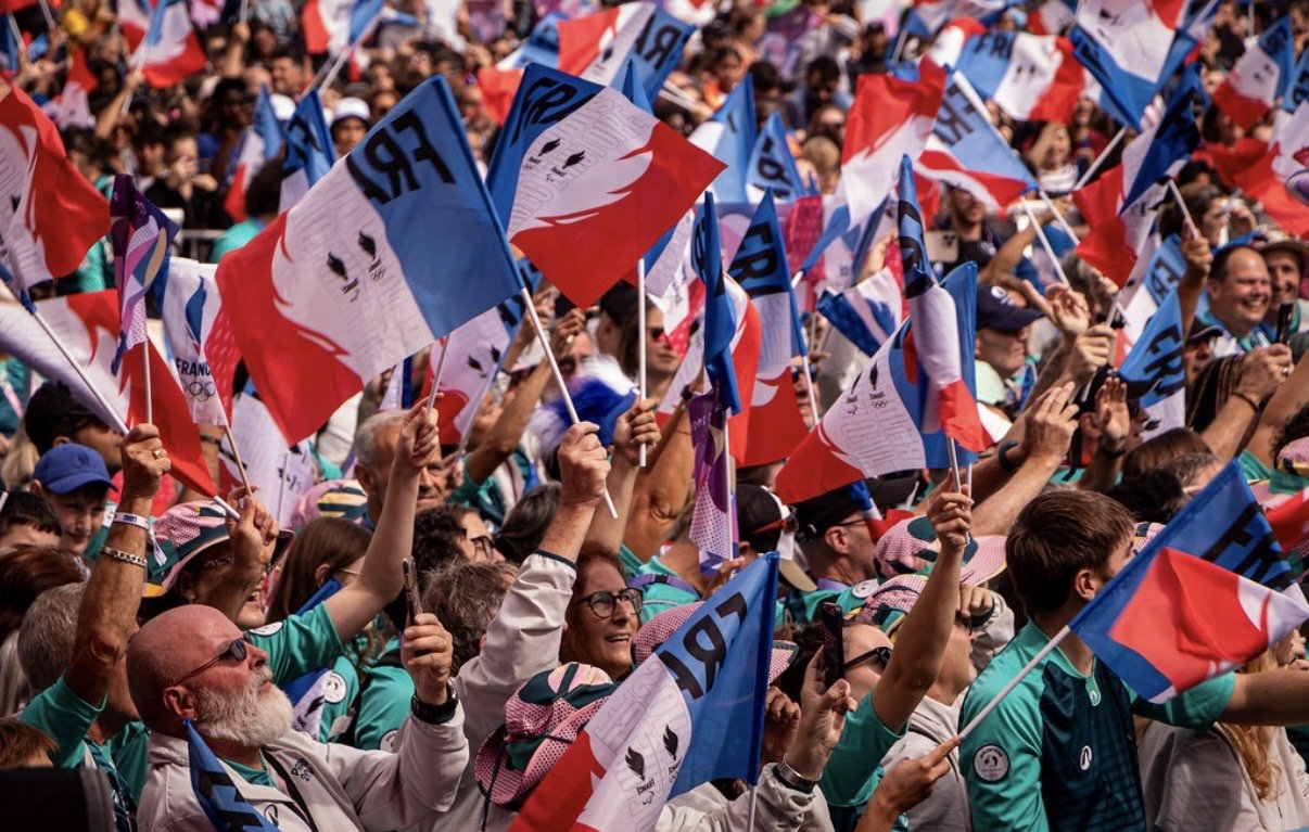 Photographie d'une foule de personnes en Seine-Saint-Denis tenant des drapeaux français lors d'un rassemblement public pour la fin des jeux olympiques et paralympiques 2024 à La Courneuve. 