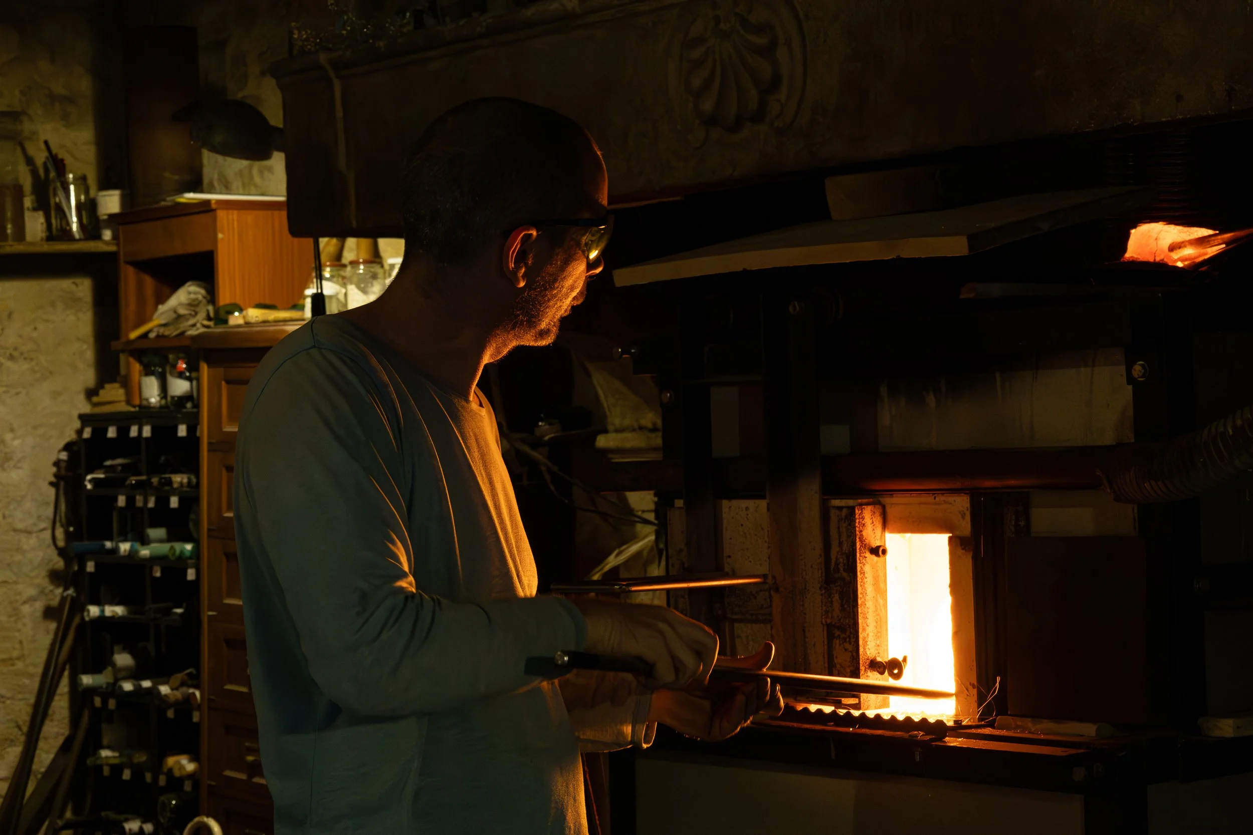 Photographie d'un artiste verrier travaillant dans un atelier, utilisant des outils pour travailler le verre sur une pièce en fusion dans un four à haute température.