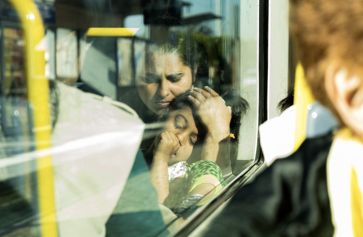 Photographie d'une femme et sa fillette dans un tramway en Seine-Saint-Denis. La lumière est très vive et colorée, la petite fille semble endormie, vue à travers la vitre comme un reflet. 
