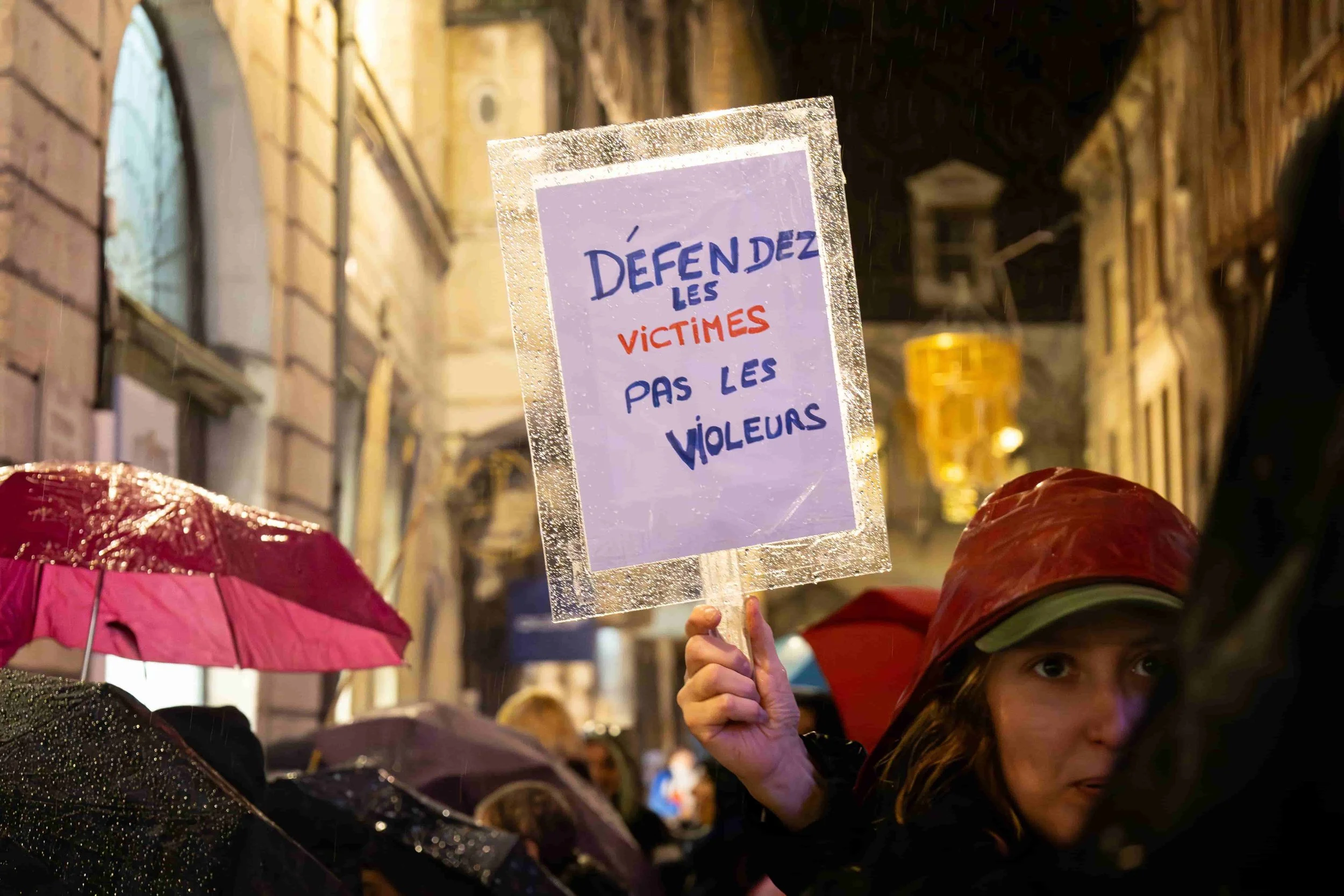 Photographie d'une femme tenant une pancarte lors d'une manifestation nocturne sous la pluie à Dijon. La pancarte dit 'Défendez les victimes, pas les violeurs', une manifestation contre les violences sexistes et sexuelles faites aux femmes. 