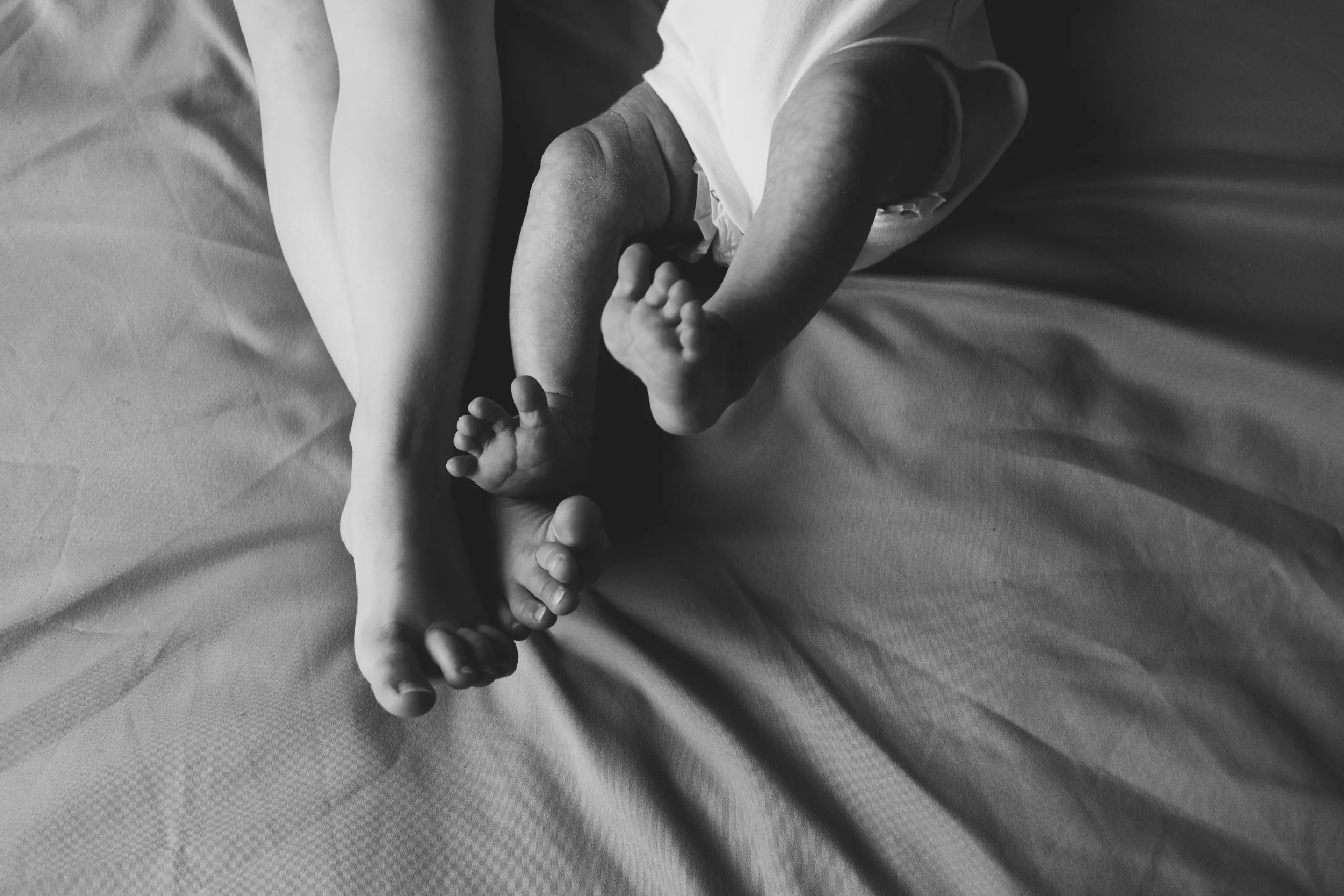 Black and white photo of a woman lying on a bed with a young child, their feet intertwined.
