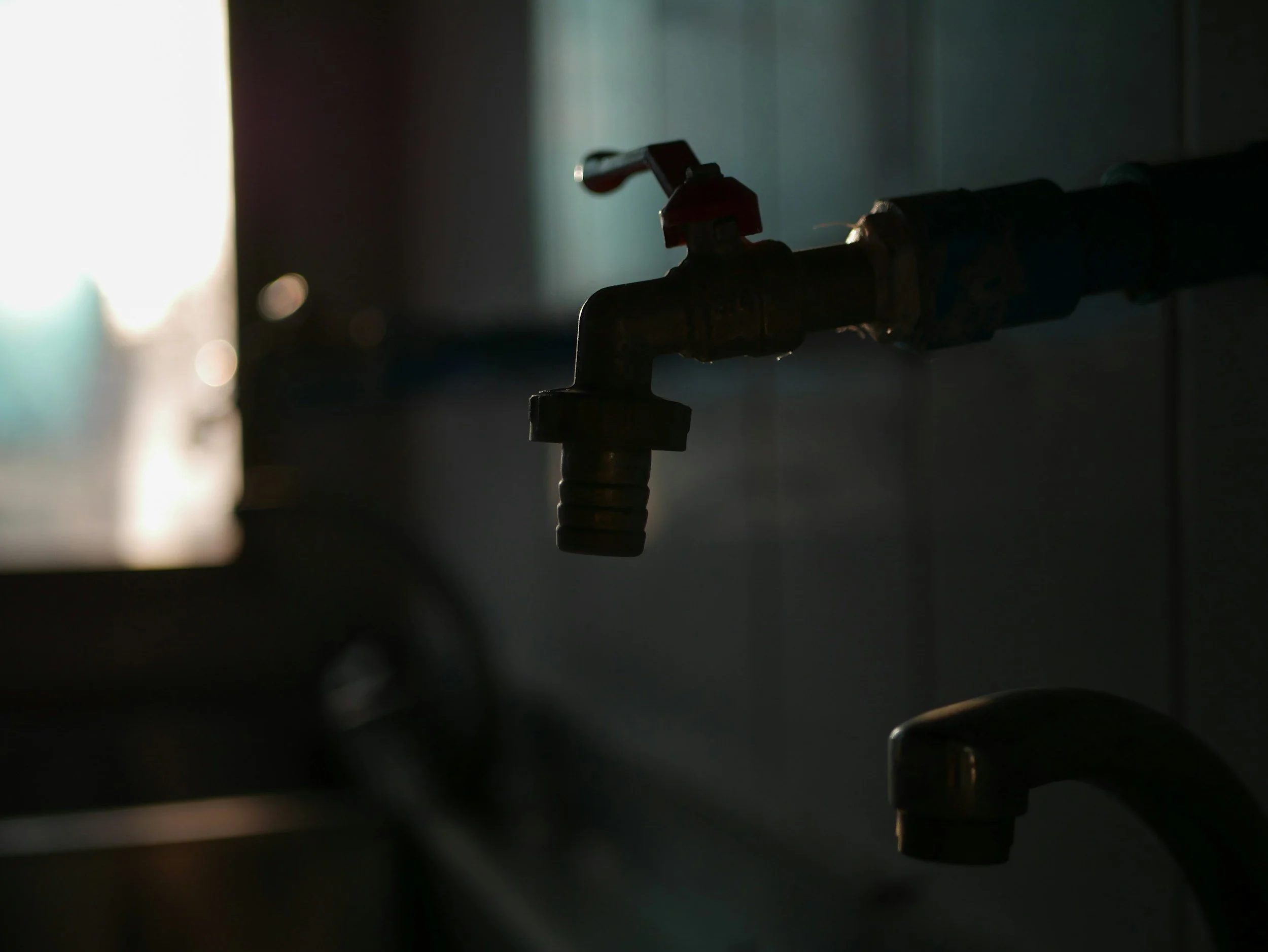 Close-up of a metal water valve pipe in a dark room, with a light source in the background.