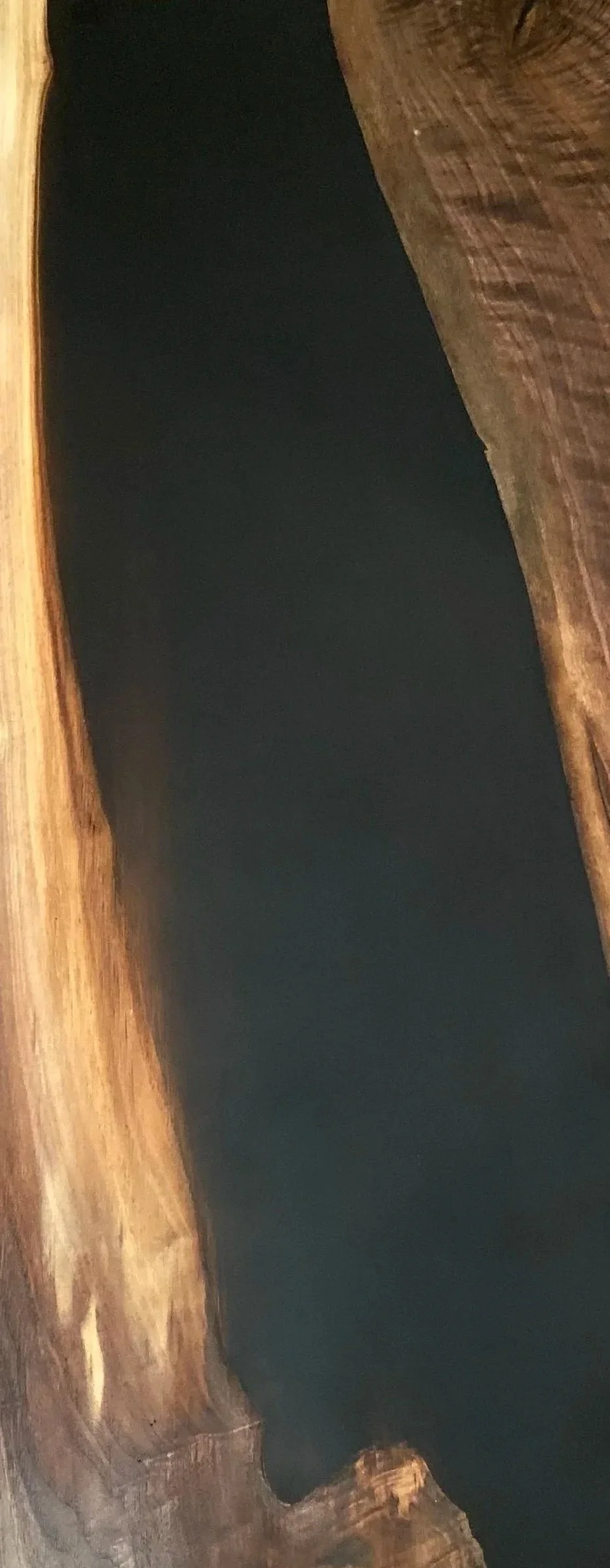 Close-up of a dark, smooth surface partially surrounded by textured, weathered wooden edges.