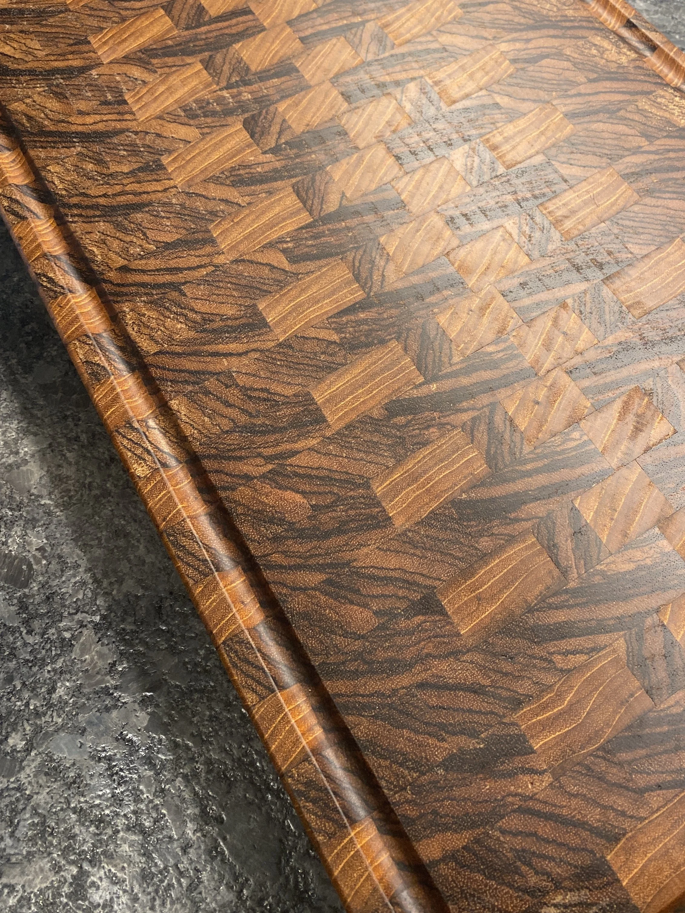 Close-up of a wooden table with a parquet pattern, featuring alternating light and dark wood pieces and a rounded edge.