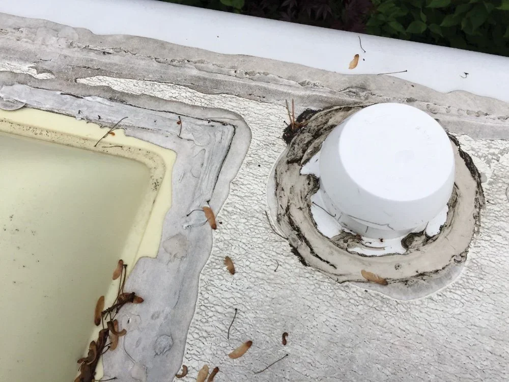 Close-up of a roof vent pipe surrounded by peeling paint and a sunroof with dirt and debris.