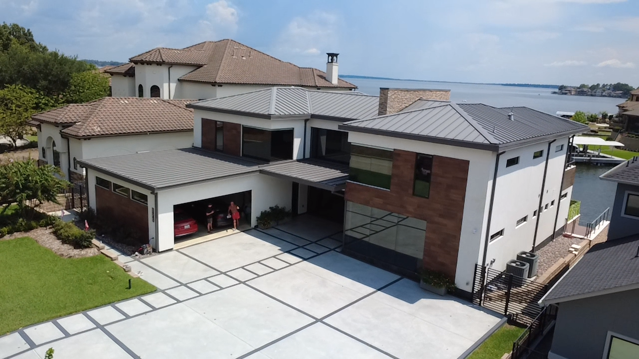 Modern house with a drive-thru garage, located near water, with a large driveway and landscaped yard.