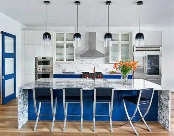Modern kitchen with white upper cabinets, blue lower cabinets, a marble island with seating, pendant lights, and stainless steel appliances.