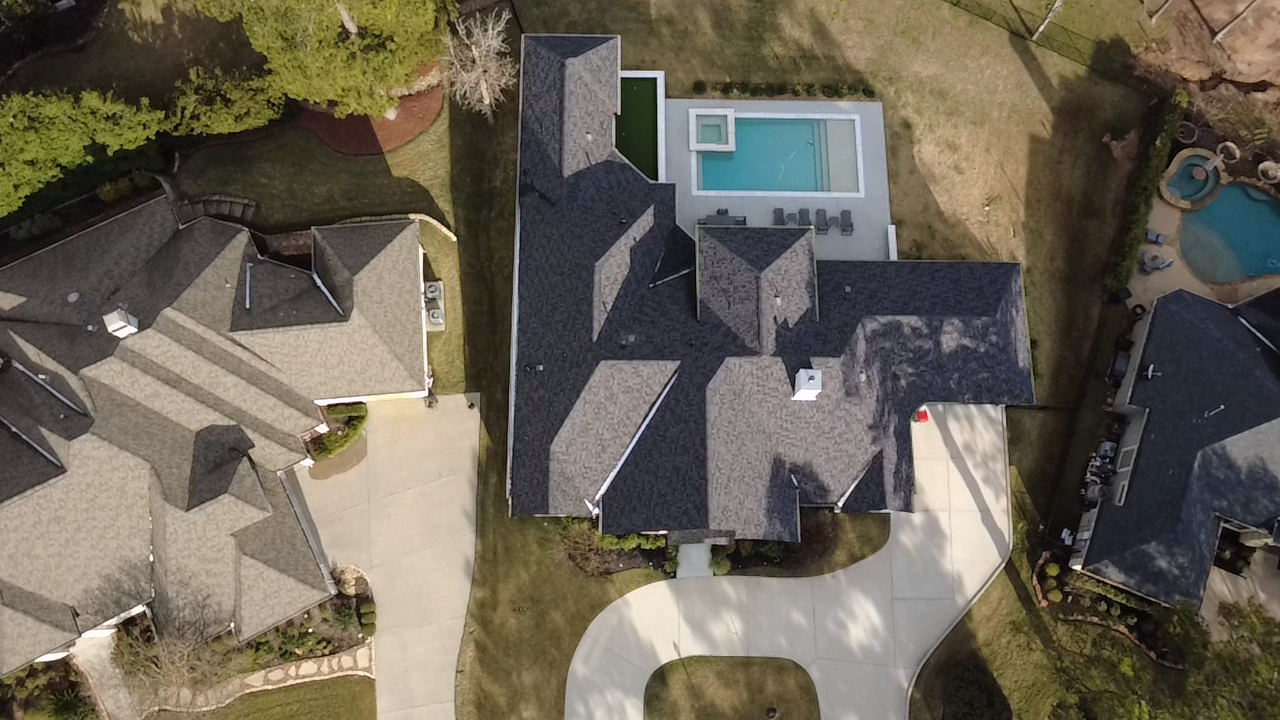 An aerial view of three houses in a suburban neighborhood, with one house featuring a swimming pool in the backyard.