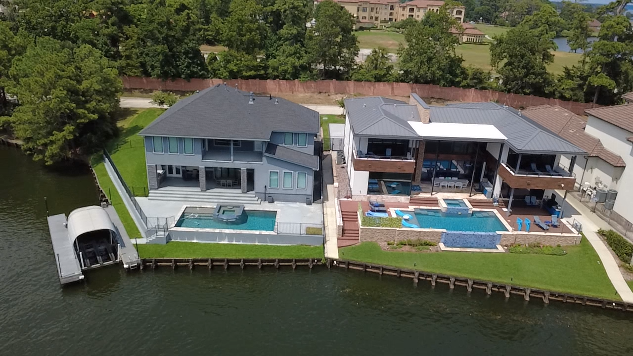 Aerial view of two modern waterfront houses with pools and docks, situated along a lake.