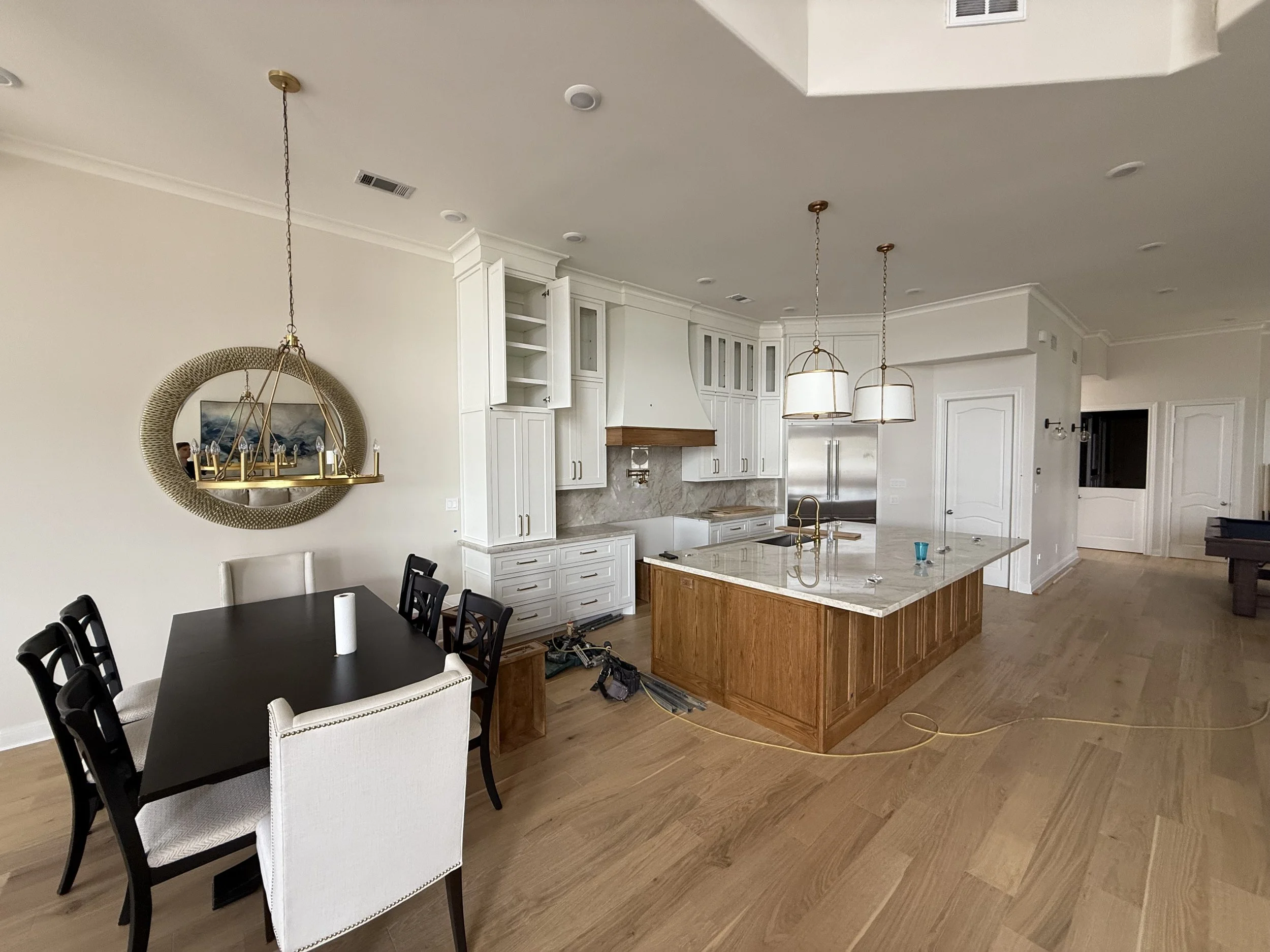 Open kitchen and dining area with white cabinets, marble countertops, a large island, hanging pendant lights, and a dining table with chairs.