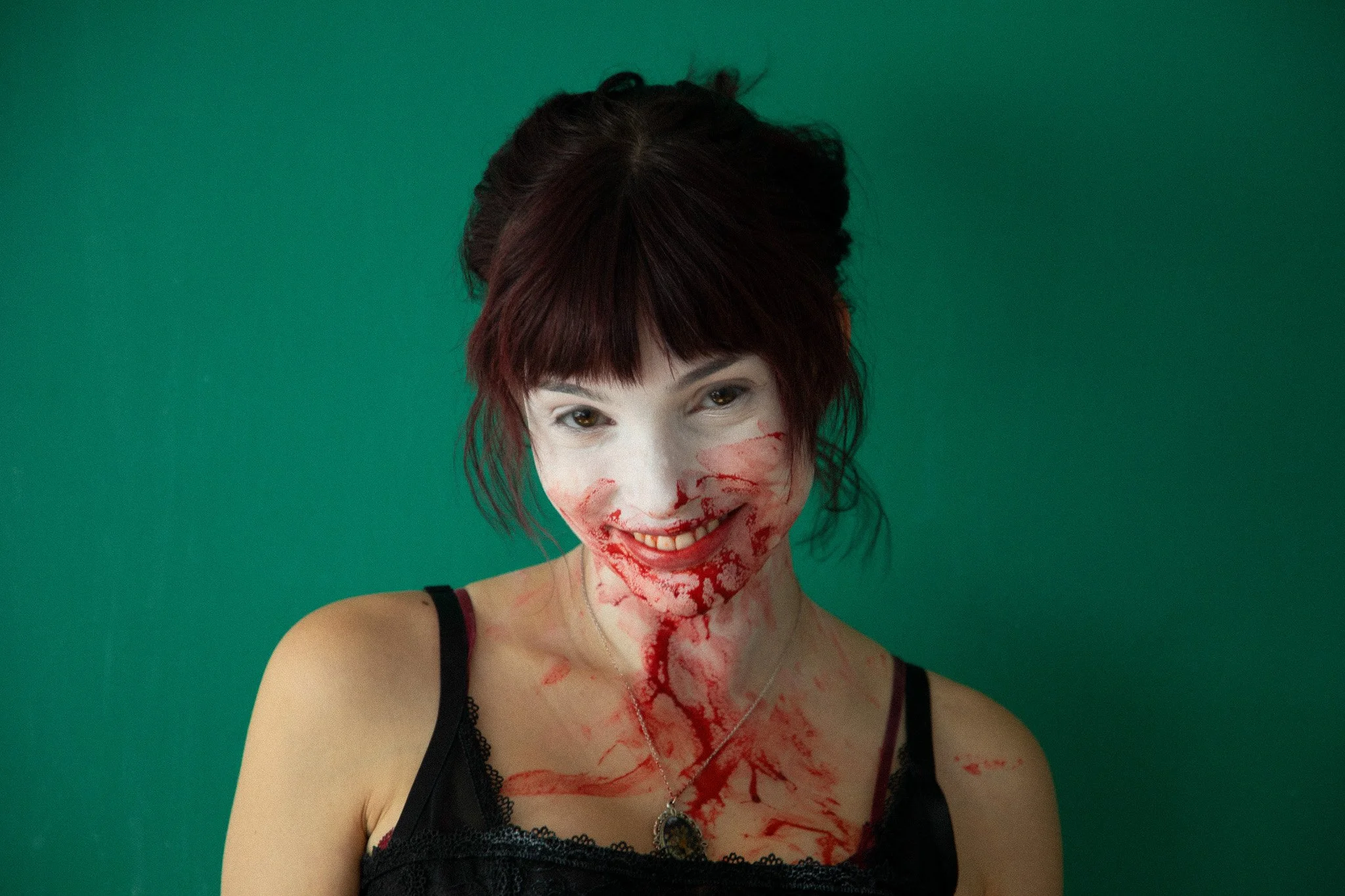 A woman with makeup resembling blood and wounds, smiling, against a green background.