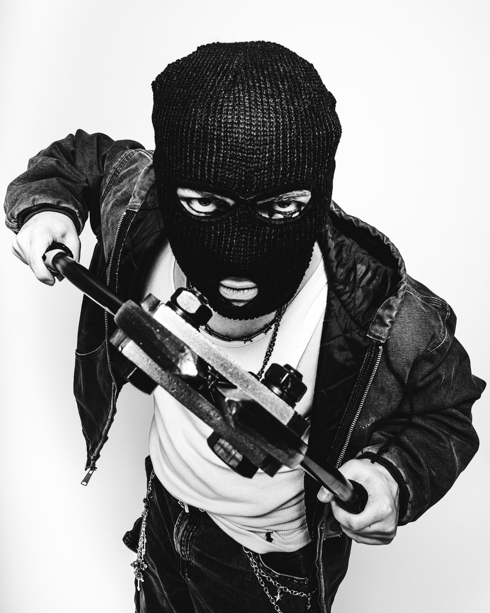 A person wearing a ski mask and dark jacket, holding a crowbar in a threatening manner, with an intense expression.