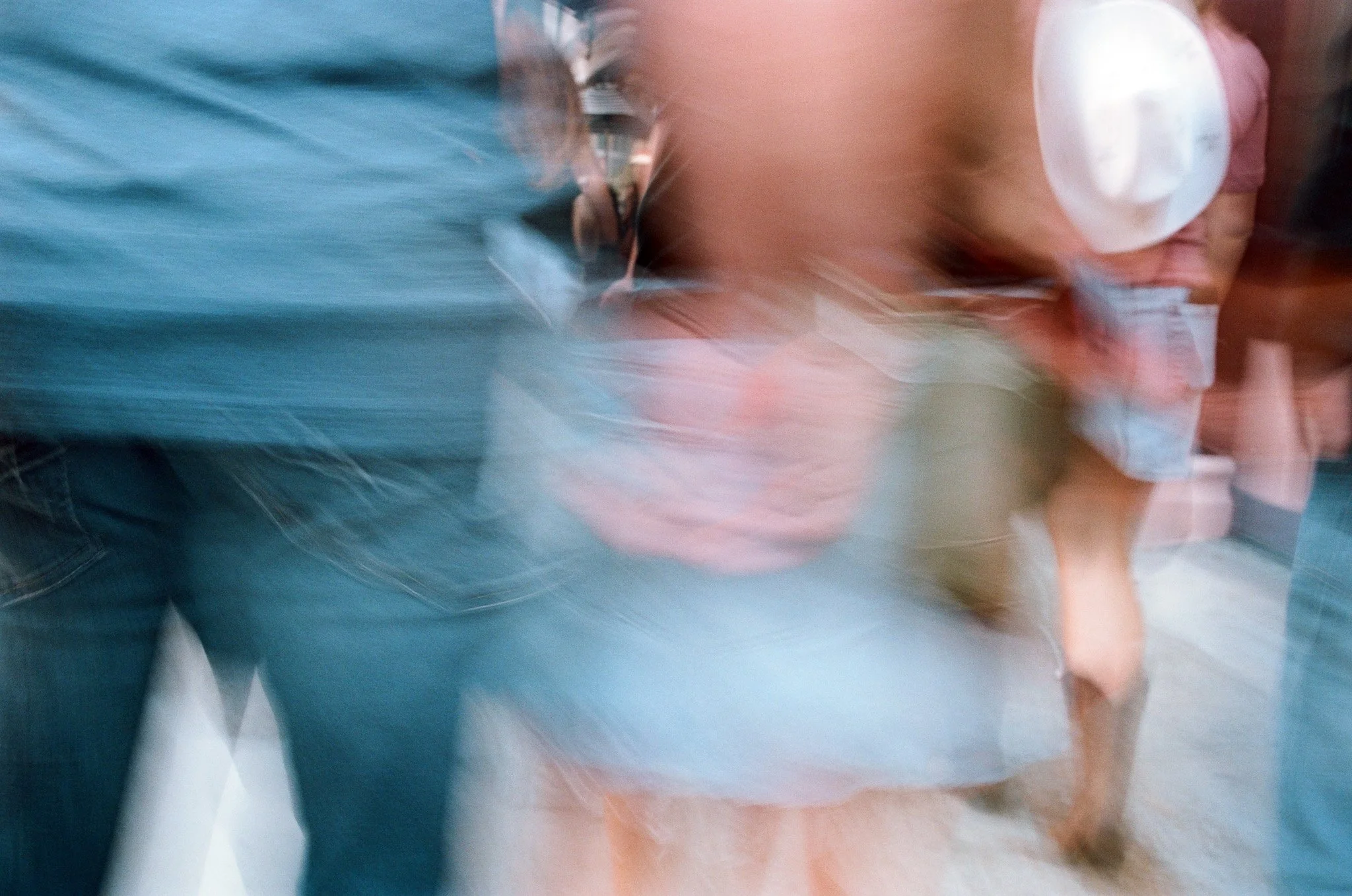 Blurred image of a woman with glasses and curly hair, wearing a light blue outfit, standing beside a person with a backpack and a teal shirt.