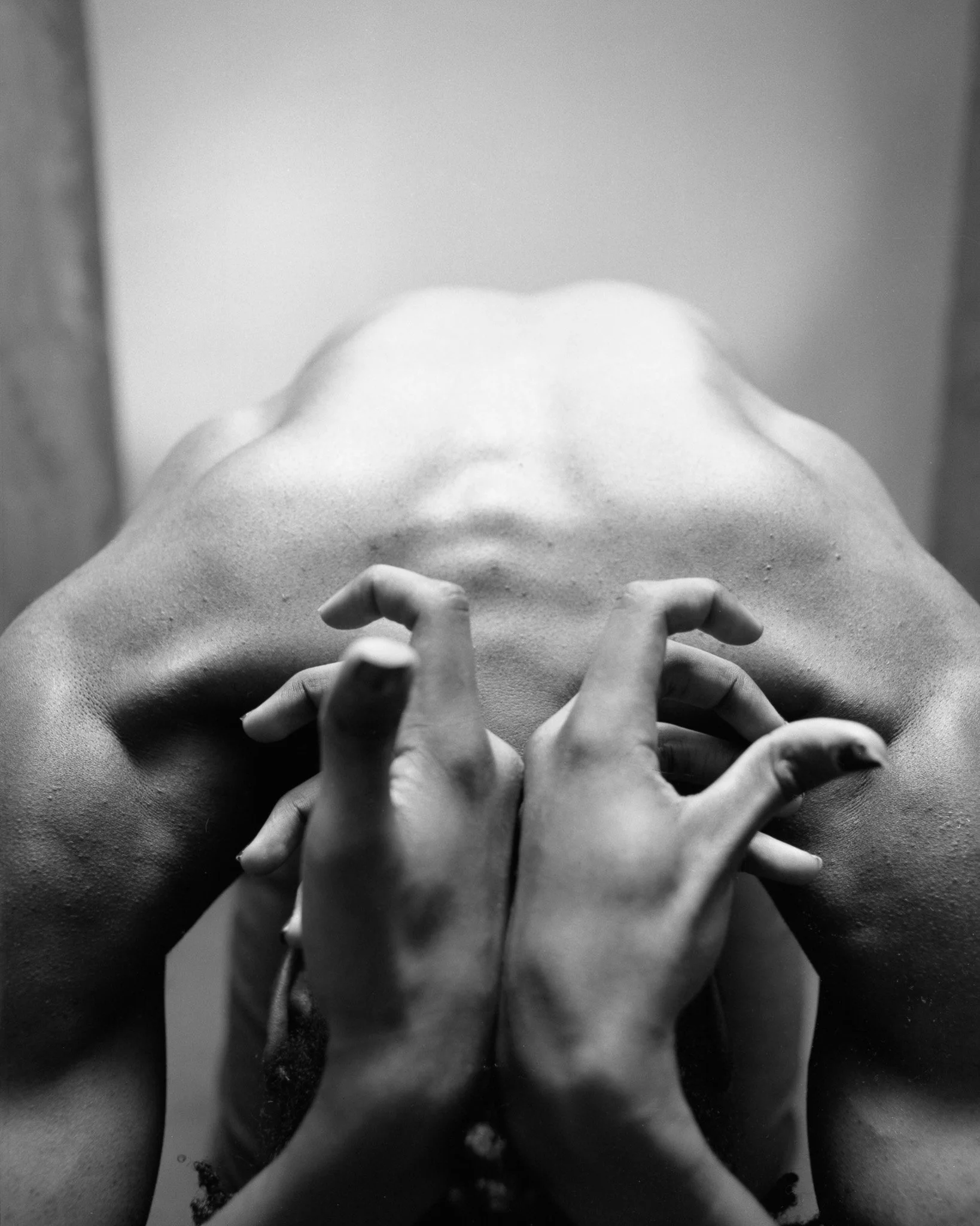 A black and white photograph of a person with their face covered by their hands, which are crossed at the wrists and positioned over their eyes, creating an abstract and artistic composition.