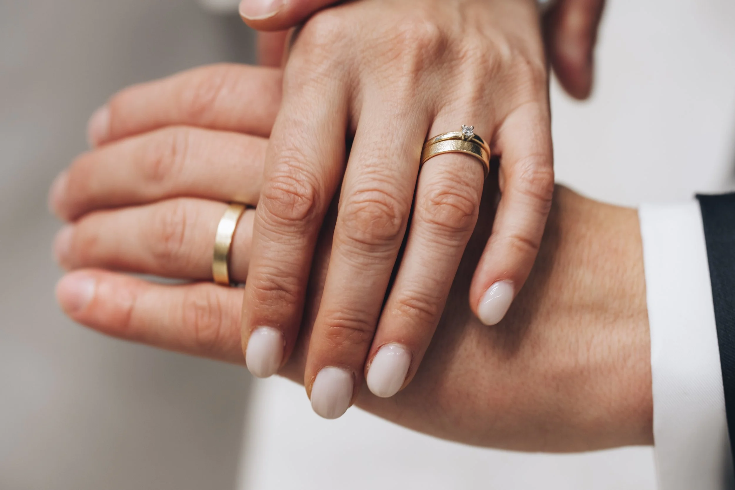 Close-up of a bride and groom holding hands, showing wedding rings on their fingers.