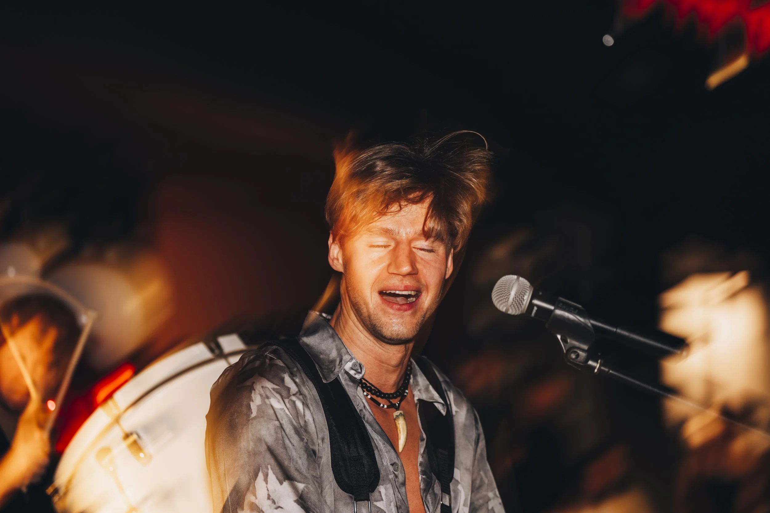 Young man singing passionately into a microphone on stage, with a blurred background and warm lighting.