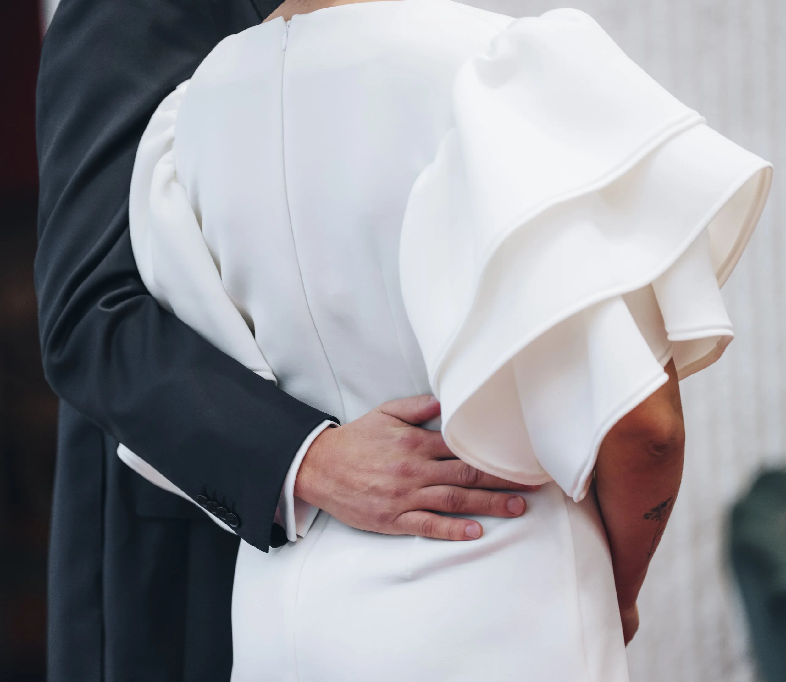 Close-up of a groom and bride holding hands during their wedding ceremony, showing part of their formal attire.