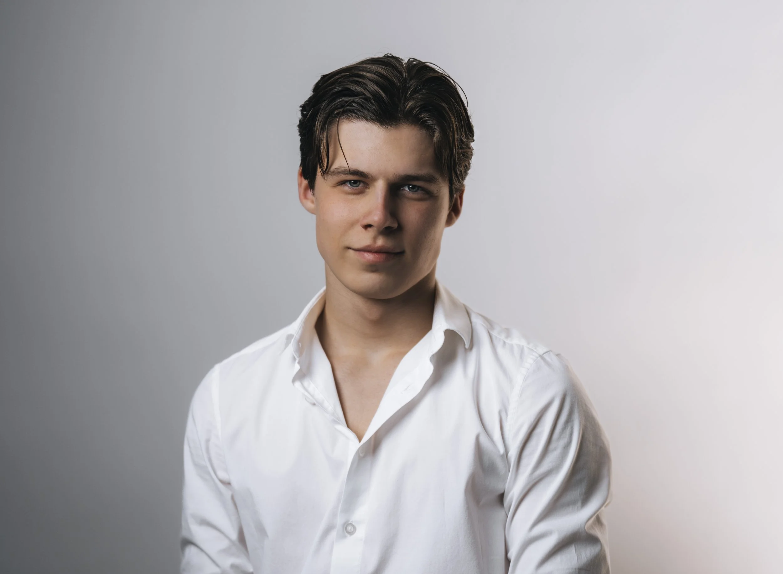 Young man with dark hair in a white shirt against a neutral background.