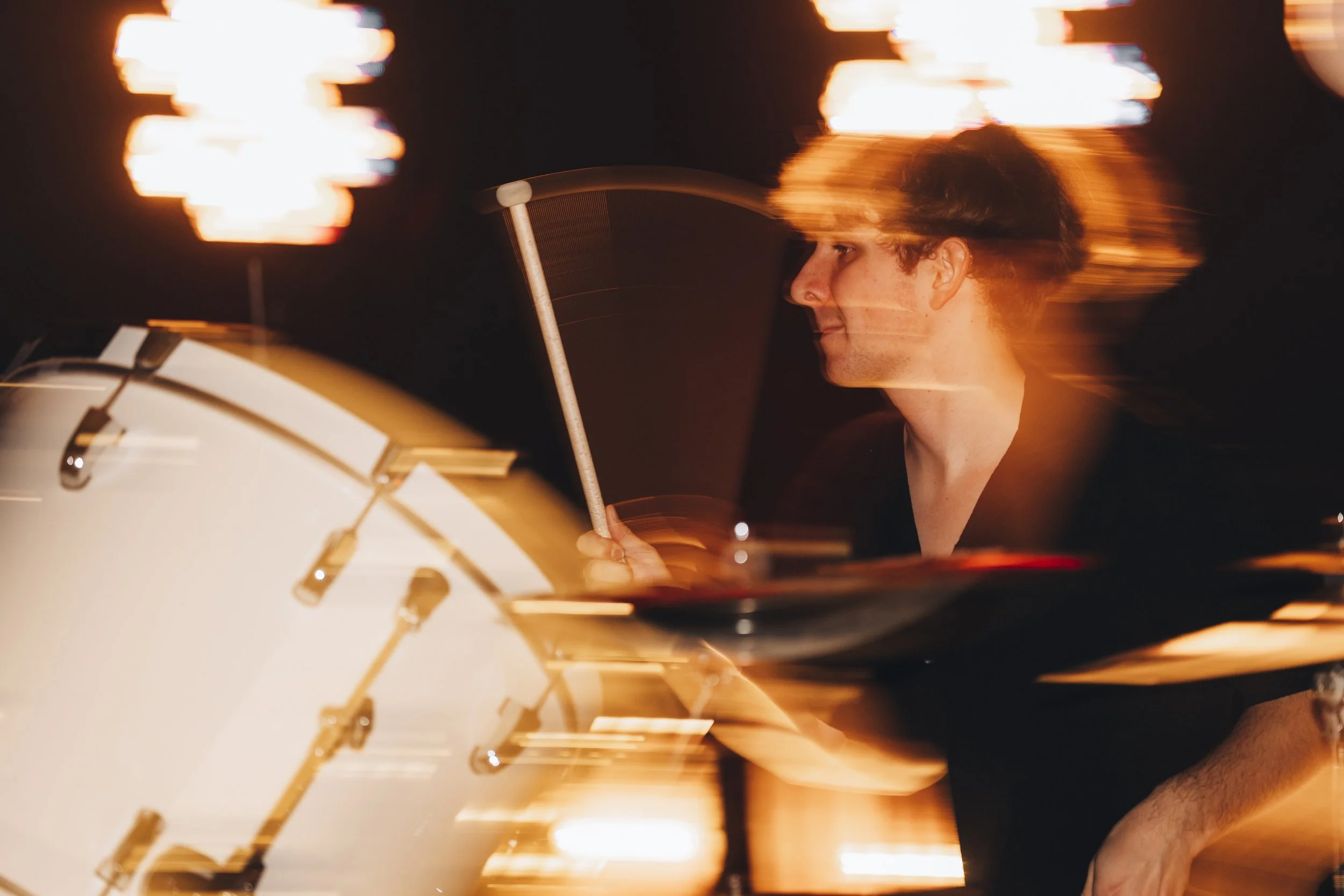 A person playing drums at night with motion blur and bright light reflections.