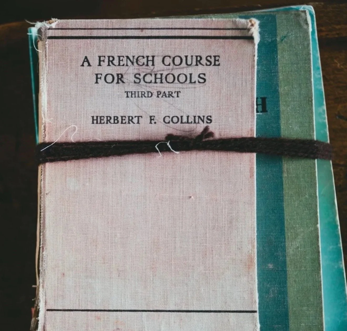 A stack of vintage books, with the top one titled 'A French Course for Schools Third Part' by Herbert F. Collins, tied with a black string.
