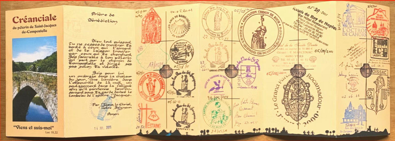 An open travel journal filled with handwritten notes, colorful stamps, and a photo of a stone bridge in a lush landscape. The journal pages contain various handwritten messages, dates, and decorative stamps from different locations.