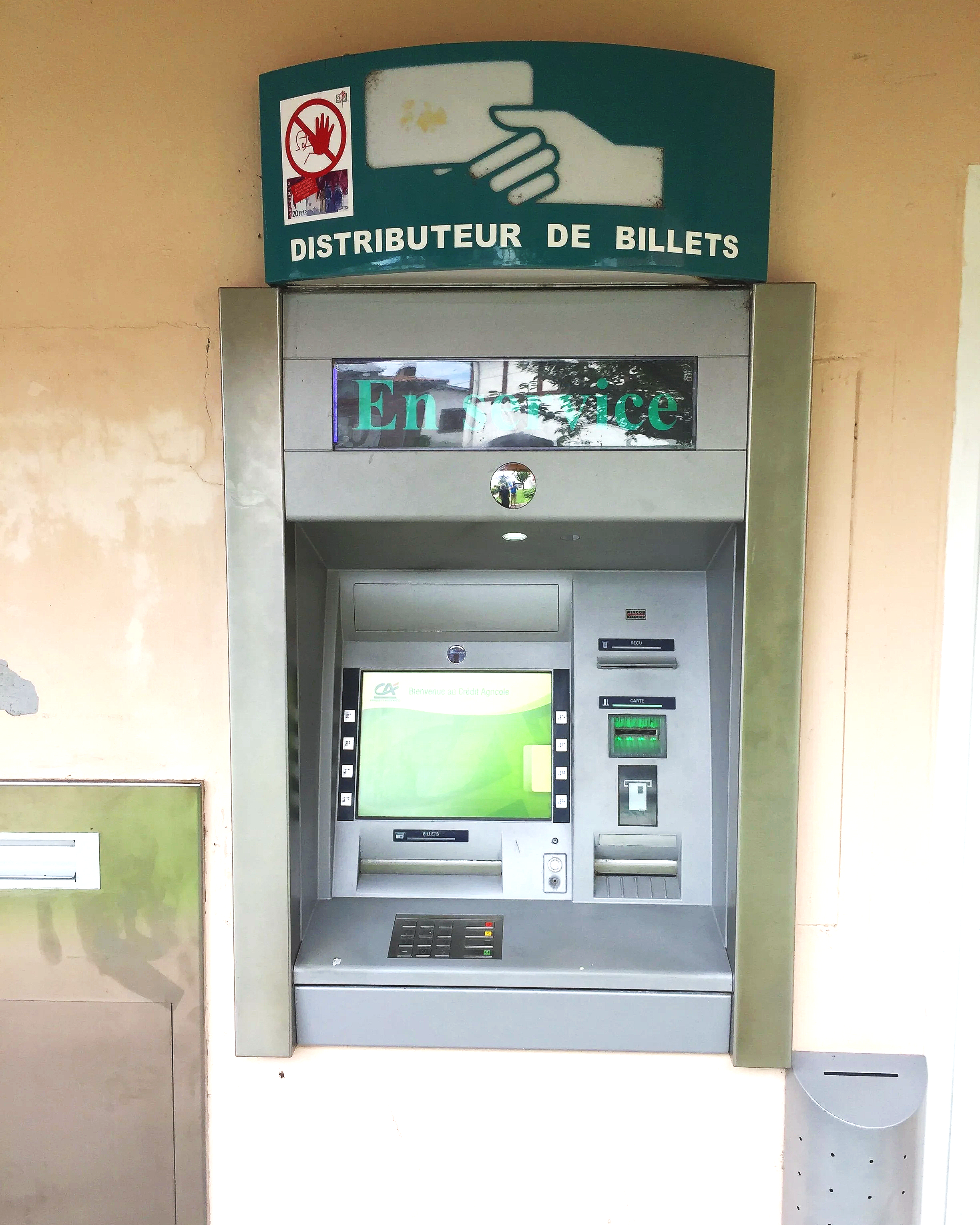 An ATM machine for ticket distribution with a sign above it showing a hand holding a smartphone, and the French words 'Distributeur de Billets'.