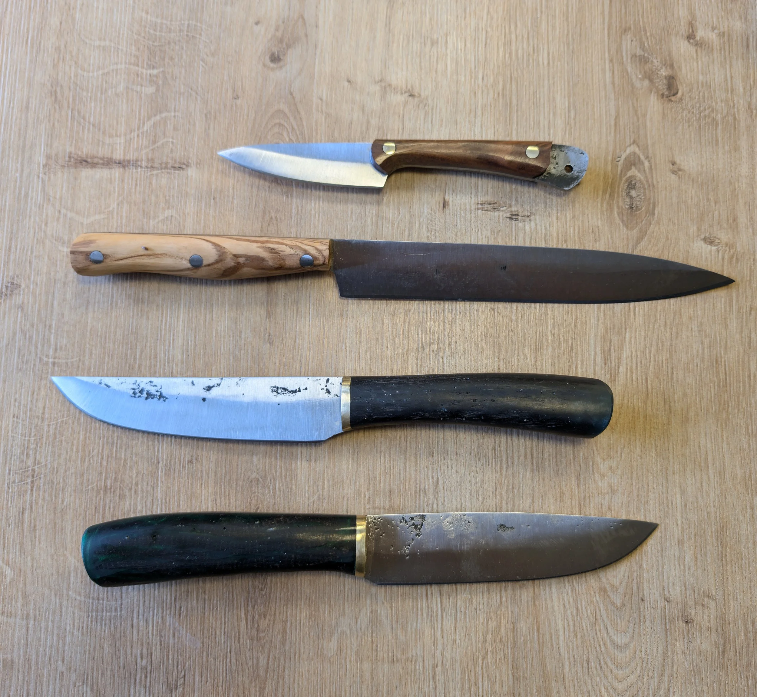 Vier Messer unterschiedlicher Größe und Design liegen ragen auf einem Holztisch.