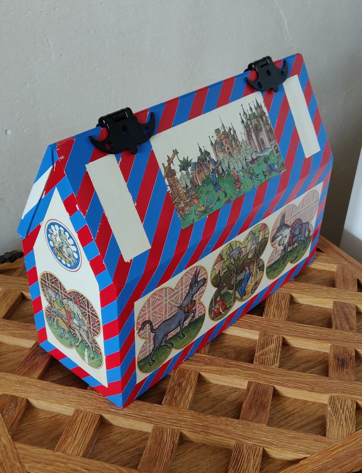 Eine bunte Truhe mit mittelalterlichen Illustrationen, verziert mit rotem und blaugemustertem Muster, steht auf einem Holztablett.
